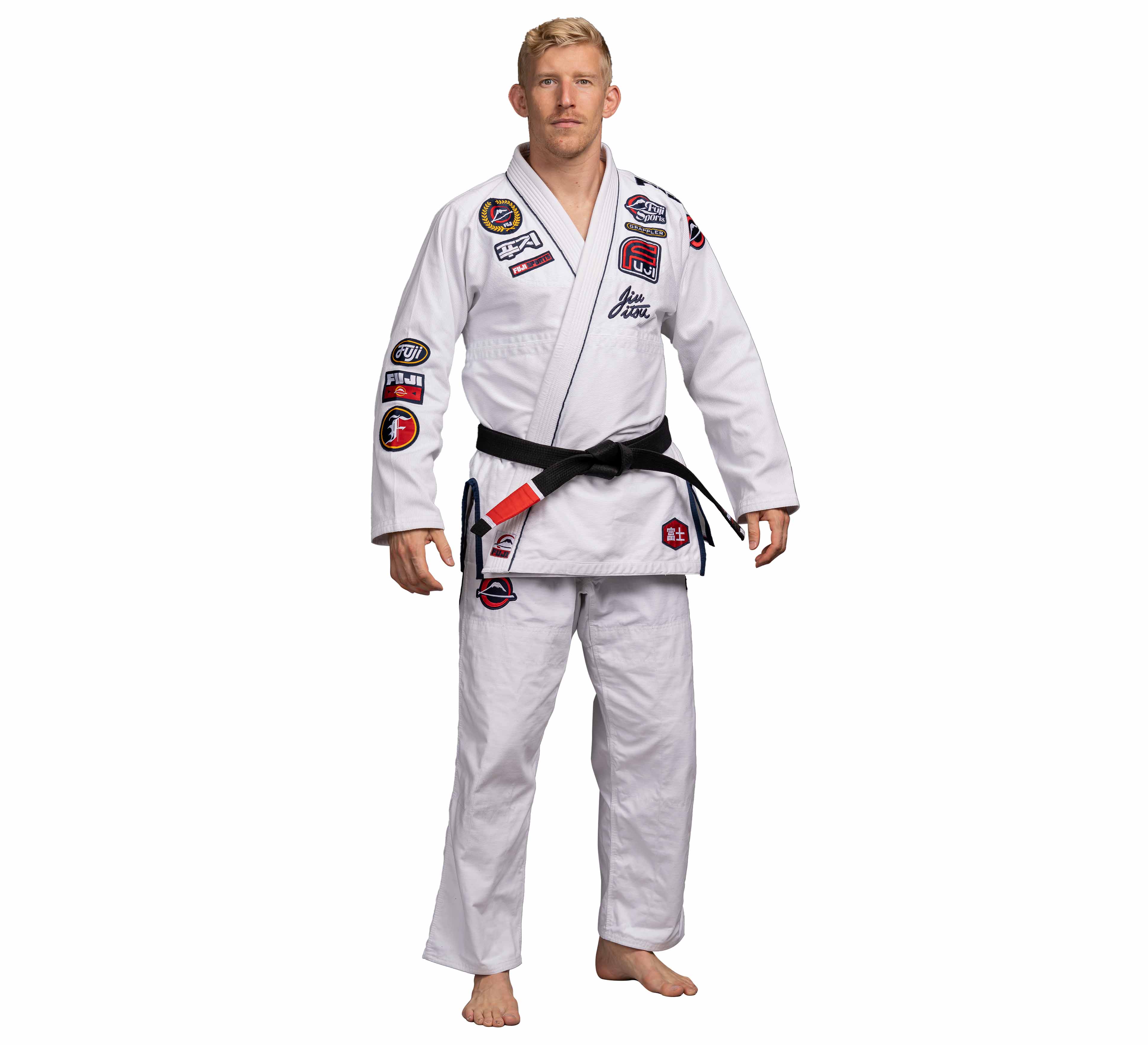 A man wearing the Suparaito BJJ Gi XTR Edition White with colorful patches and a black belt with red bar stands barefoot against a white background.