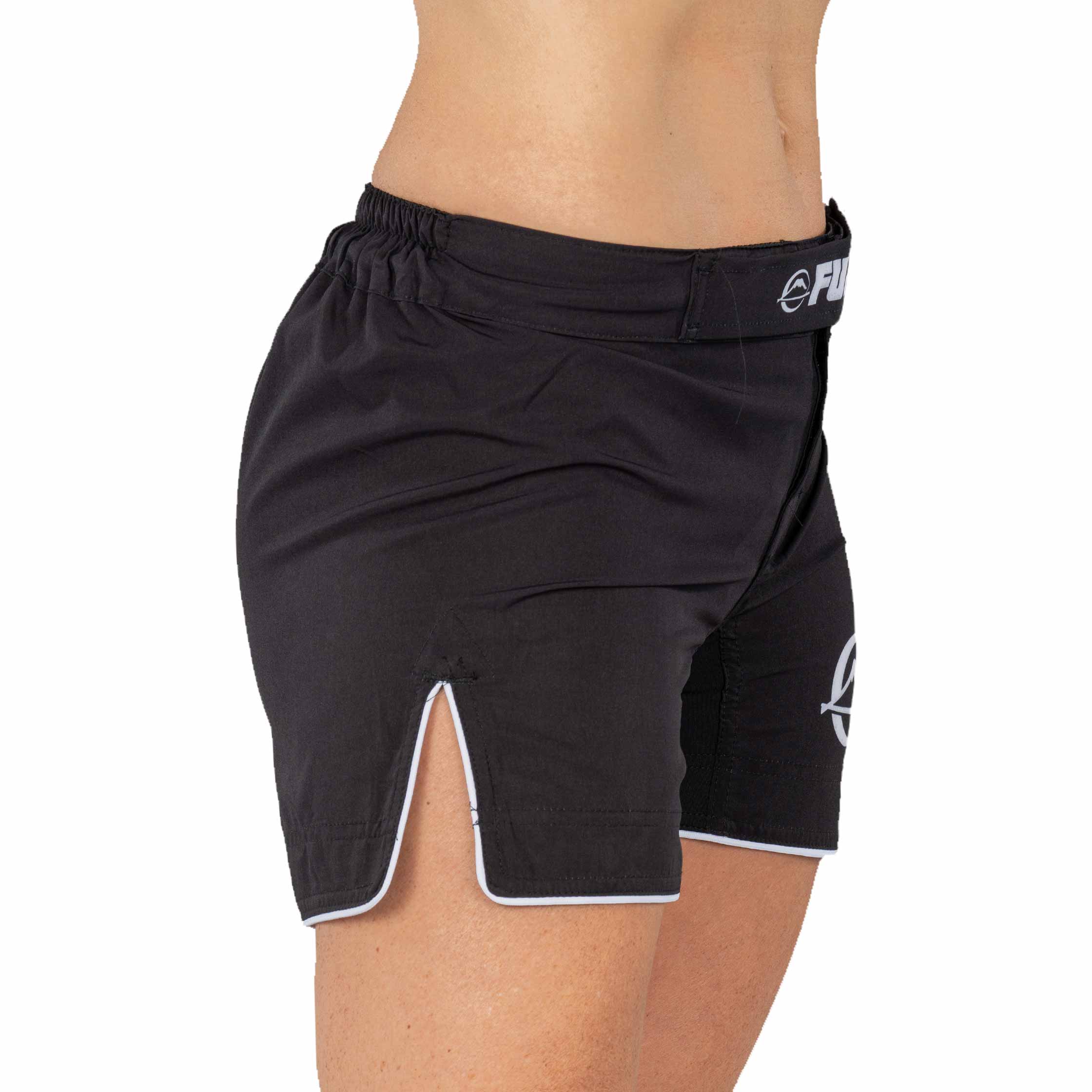 A close-up shows a person wearing Baseline Womens Black Grappling Shorts, featuring white trim and a side slit, from the waist to mid-thigh.