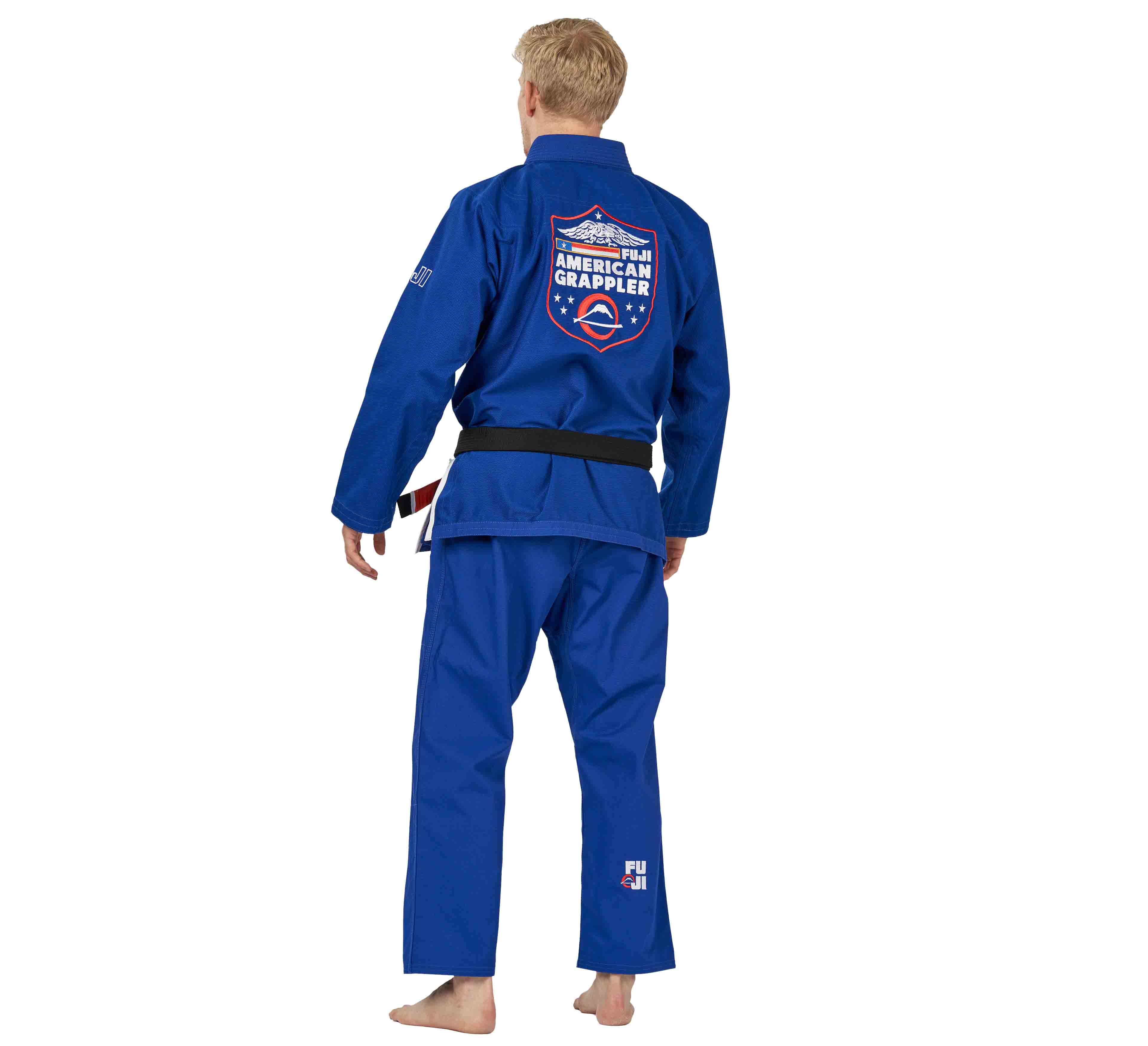 A person in the Suparaito BJJ Gi American Grappler Blue, barefoot and facing away, wears a black belt. The gi features a back patch with stars, stripes, and “American Grappler.”.