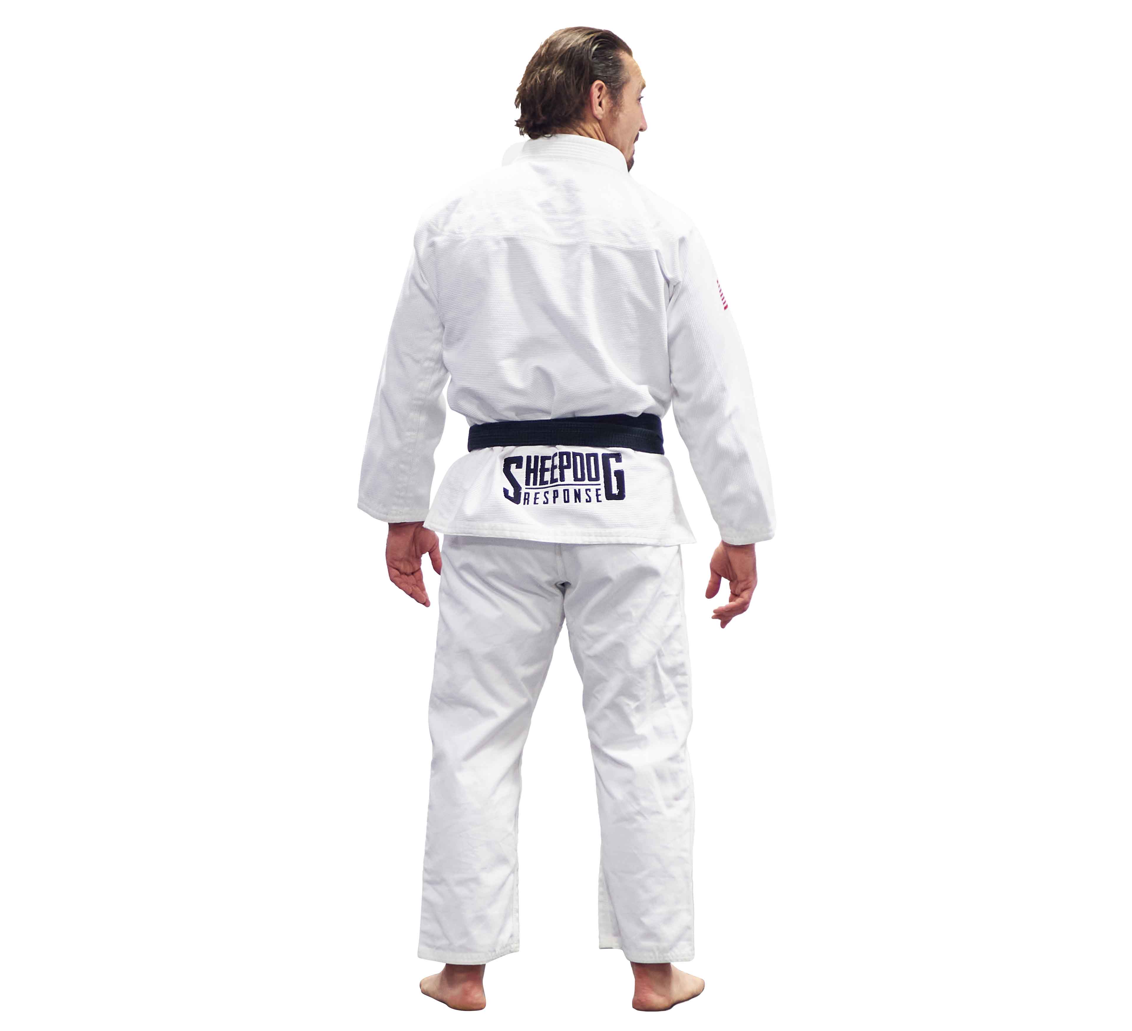 A man stands barefoot, facing away, wearing the Lightweight BJJ Gi Sheepdog Response Edition White with a black belt featuring a SHEEPDOG RESPONSE patch on the back of his uniform.