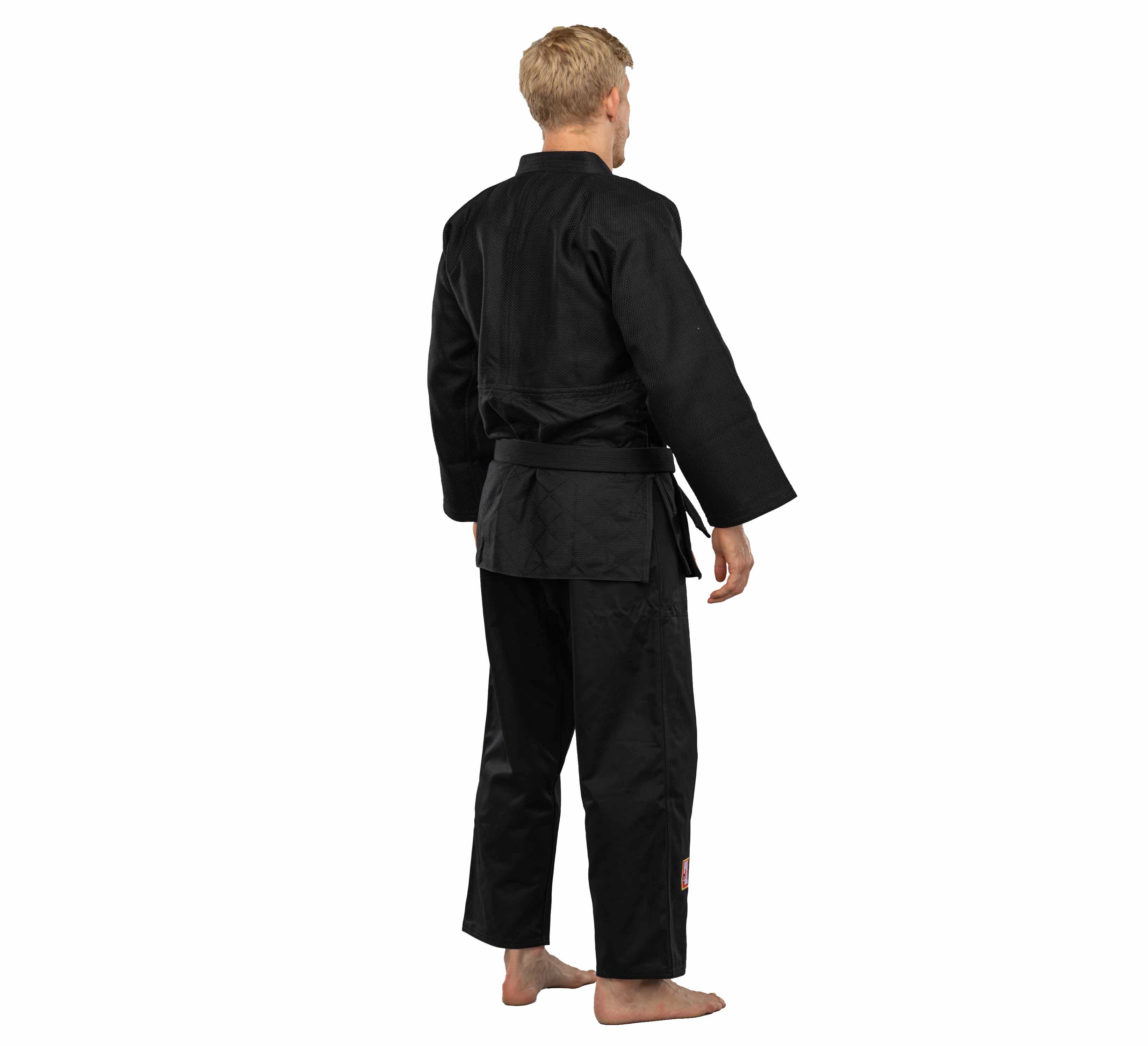 A person with short blond hair stands barefoot, facing away, wearing the Euro Competition Judo Gi Black and belt against a plain white background.