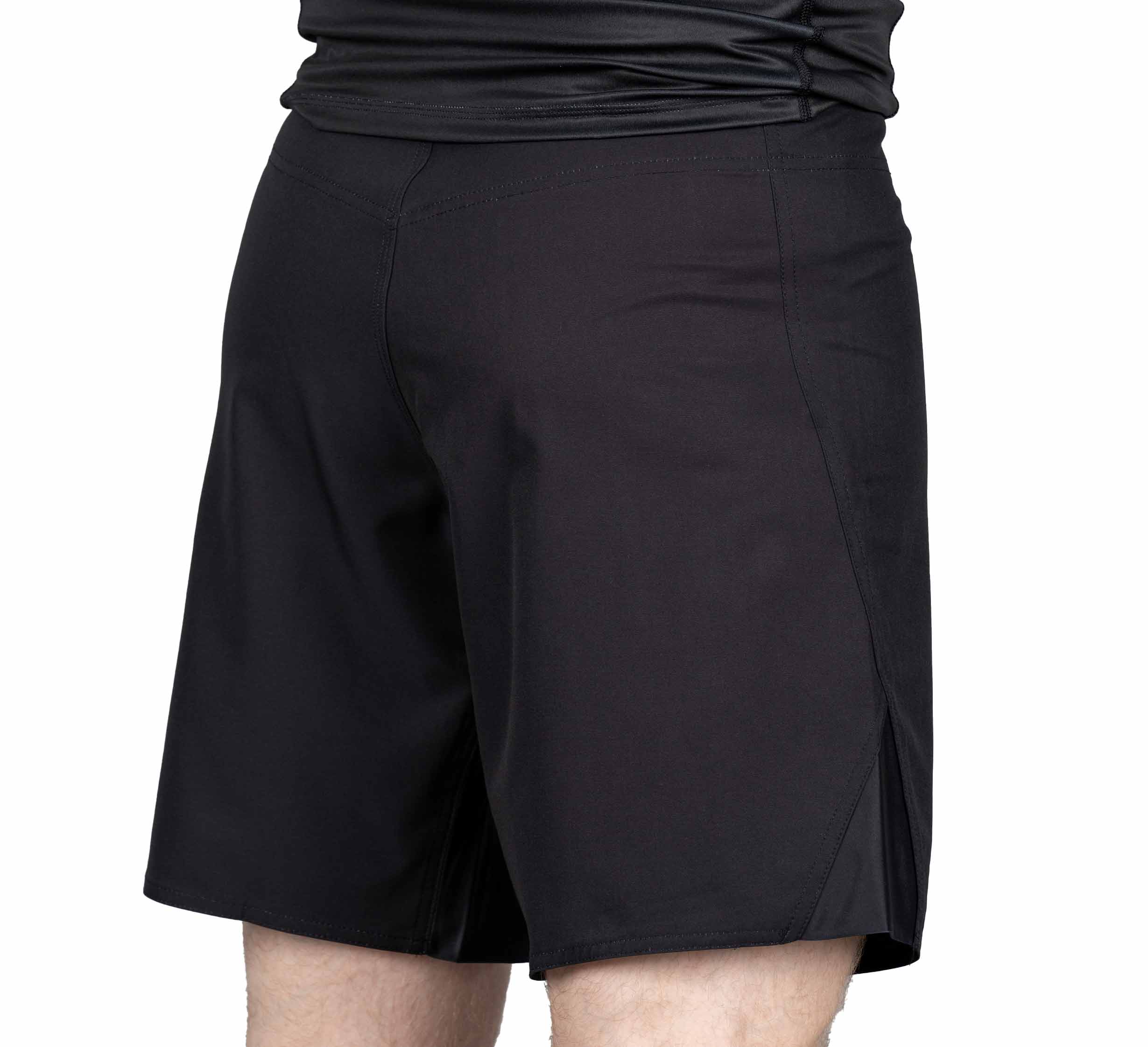 A person shown from the back and waist down is wearing Pro-Tech Grappling Fight Shorts—black, knee-length, and made of lightweight fabric.