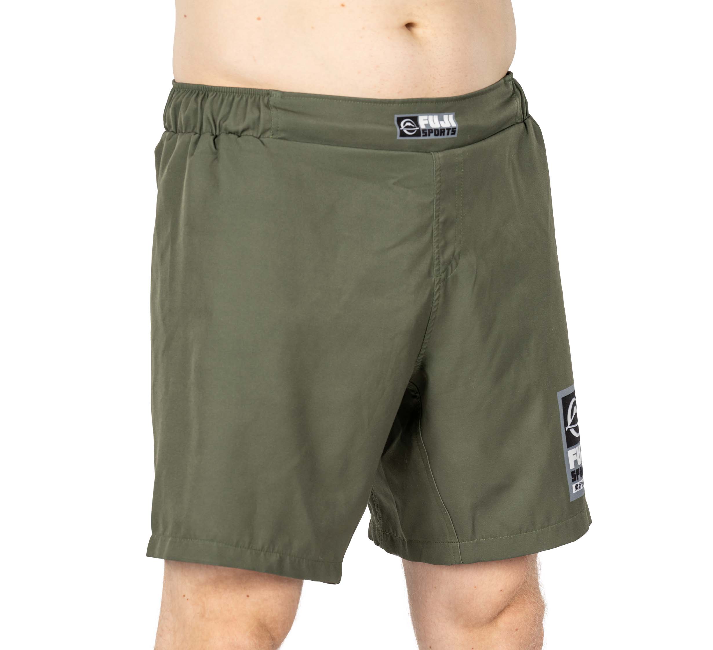 A person wearing Ultimate Grappling Shorts Military Green with an elastic waistband and Fuji Sports logo patches near the waist and lower left leg. Only the lower torso and upper legs are visible in the image.