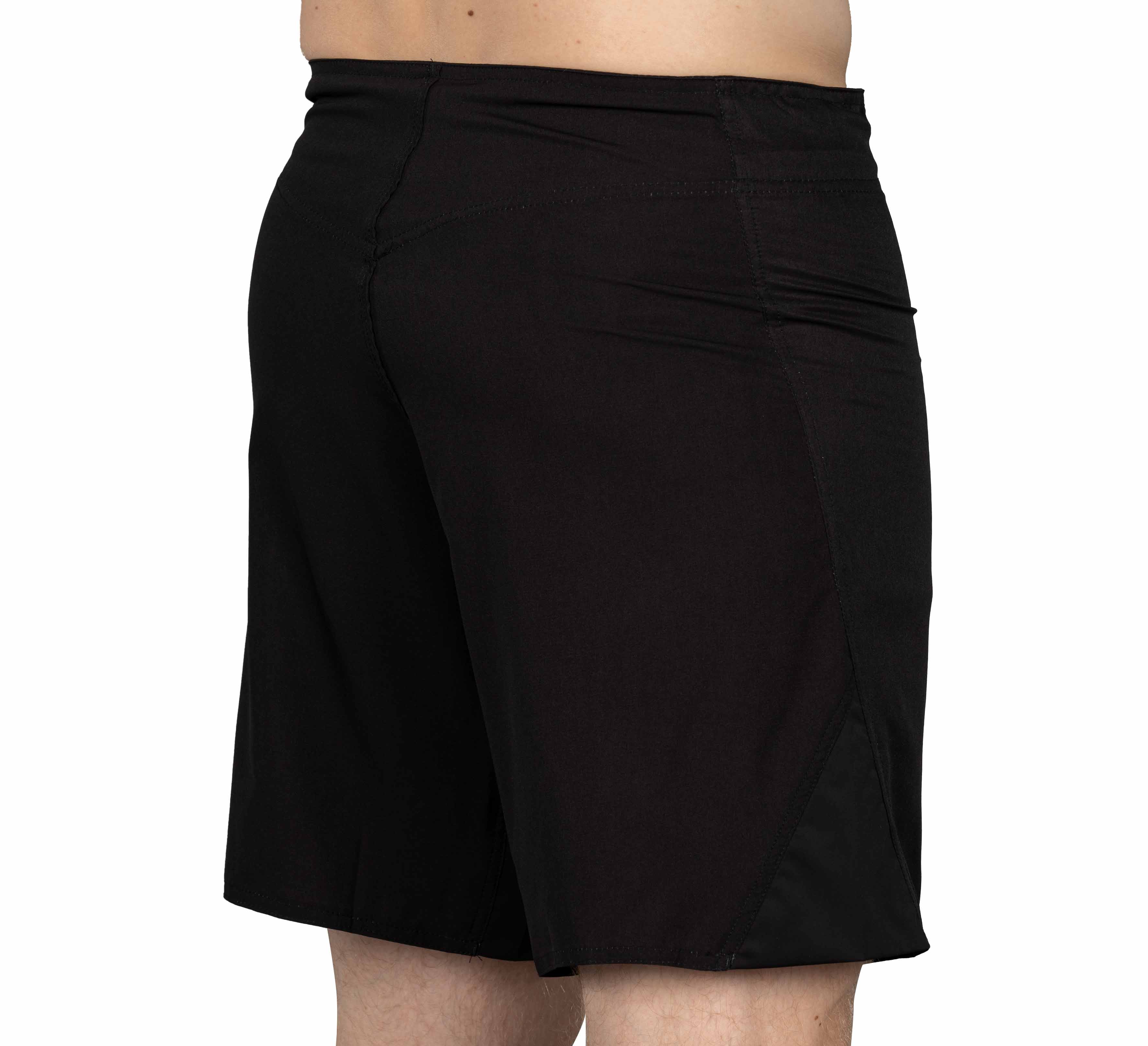 A person is seen from the back and side wearing Baseline Fight Shorts Black/Orange—knee-length athletic shorts with a simple design, shown against a plain white background. No visible logos or patterns are present.
