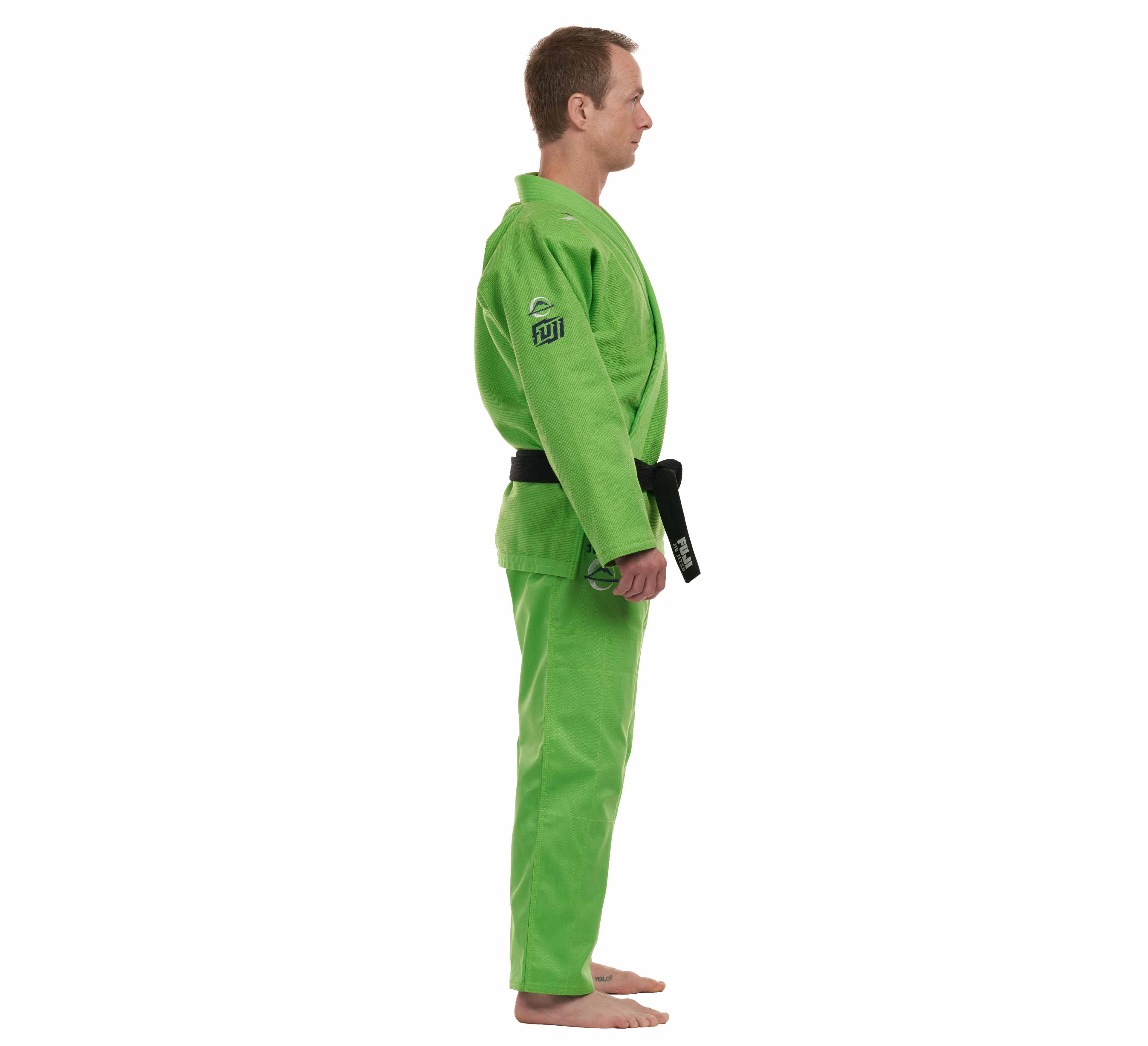 A person wearing the All Around BJJ Gi Electric Green Edition with a black belt stands barefoot in side profile against a white background.