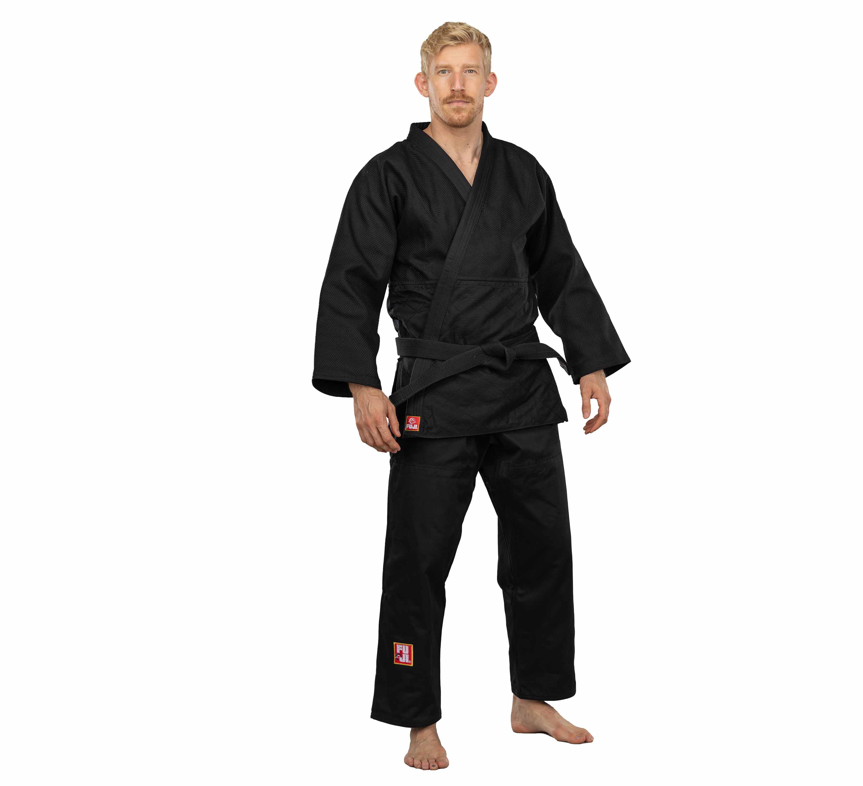 A barefoot man with short blond hair and a beard stands facing forward in a Euro Competition Judo Gi Black with a black belt, set against a plain white background.