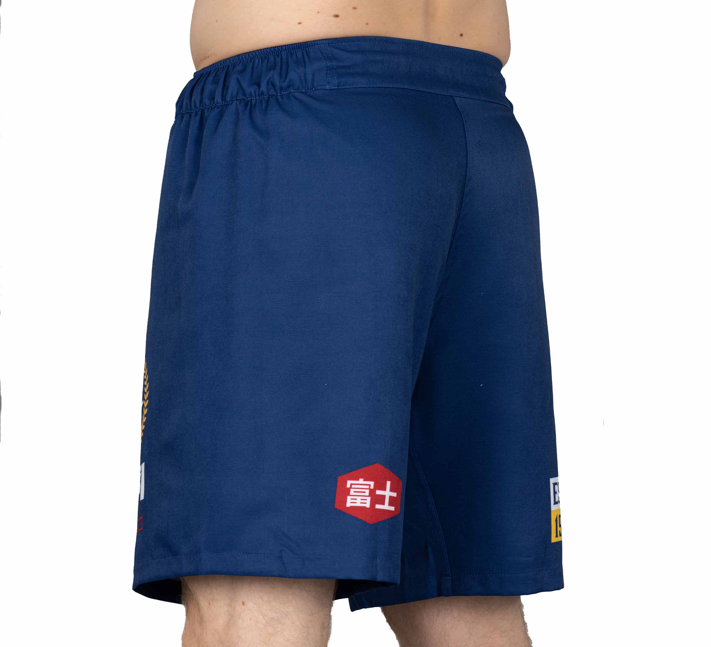 A person models the XTR Extreme Grappling Fight Shorts Navy—blue athletic shorts featuring red and white patches with Japanese writing—shown from waist to upper knee in a side view against a white background.