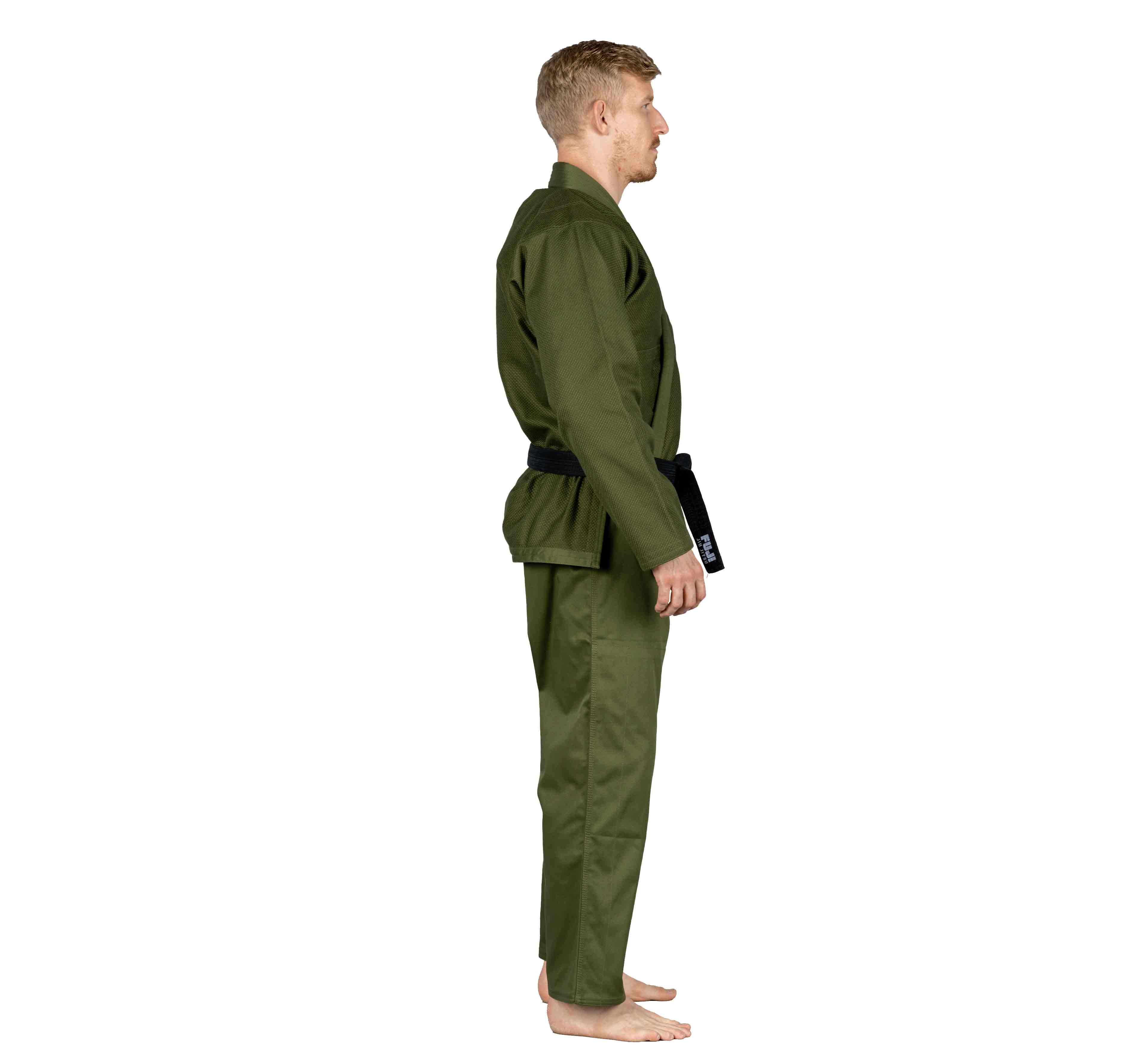 A man with short blond hair, barefoot and seen in side profile, wears the All Around BJJ Gi Military Green and a black belt against a white background.