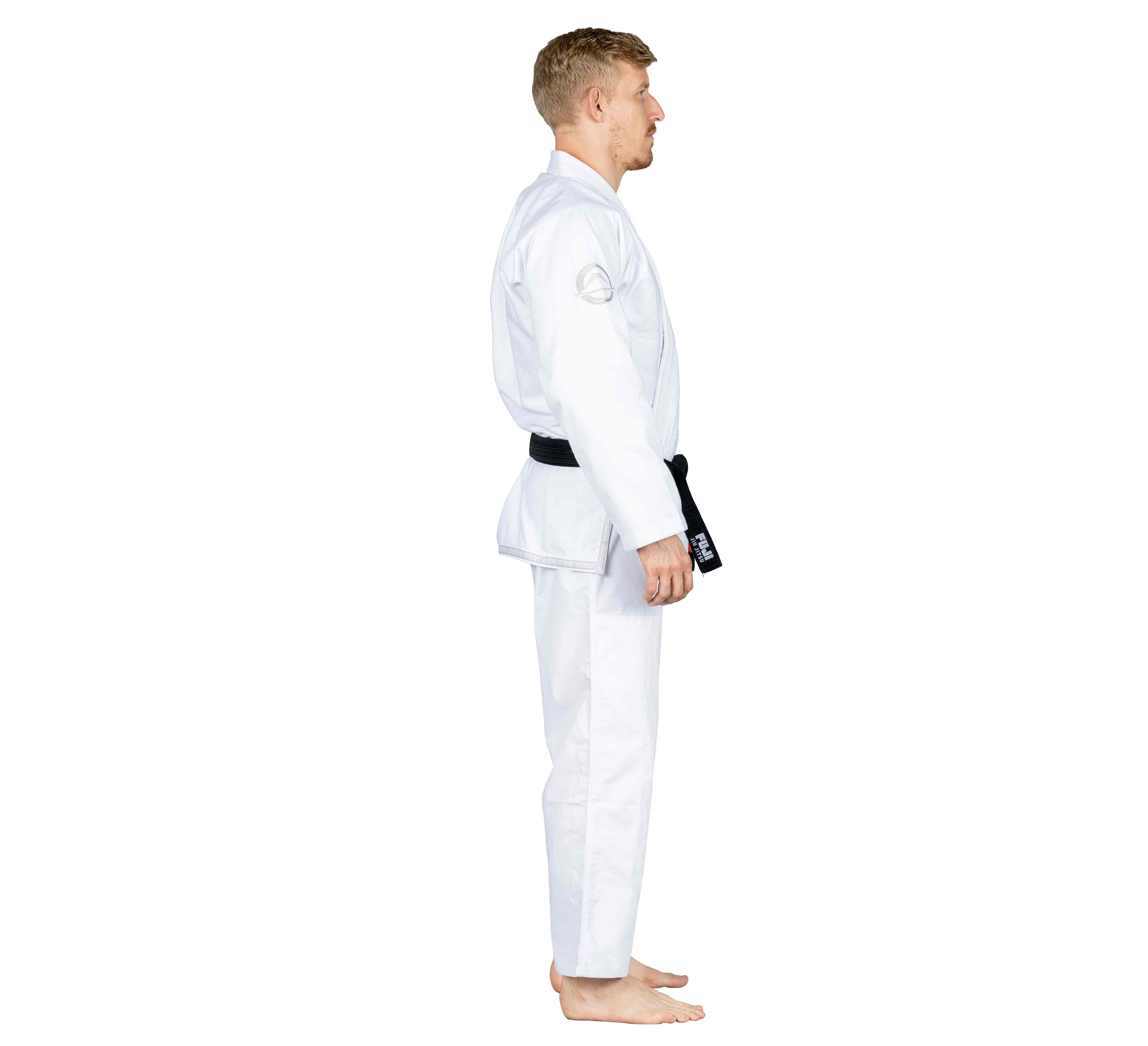 A man in the Suparaito BJJ Gi Submit Everyone Ice White and a black belt stands barefoot in side profile against a plain white background.