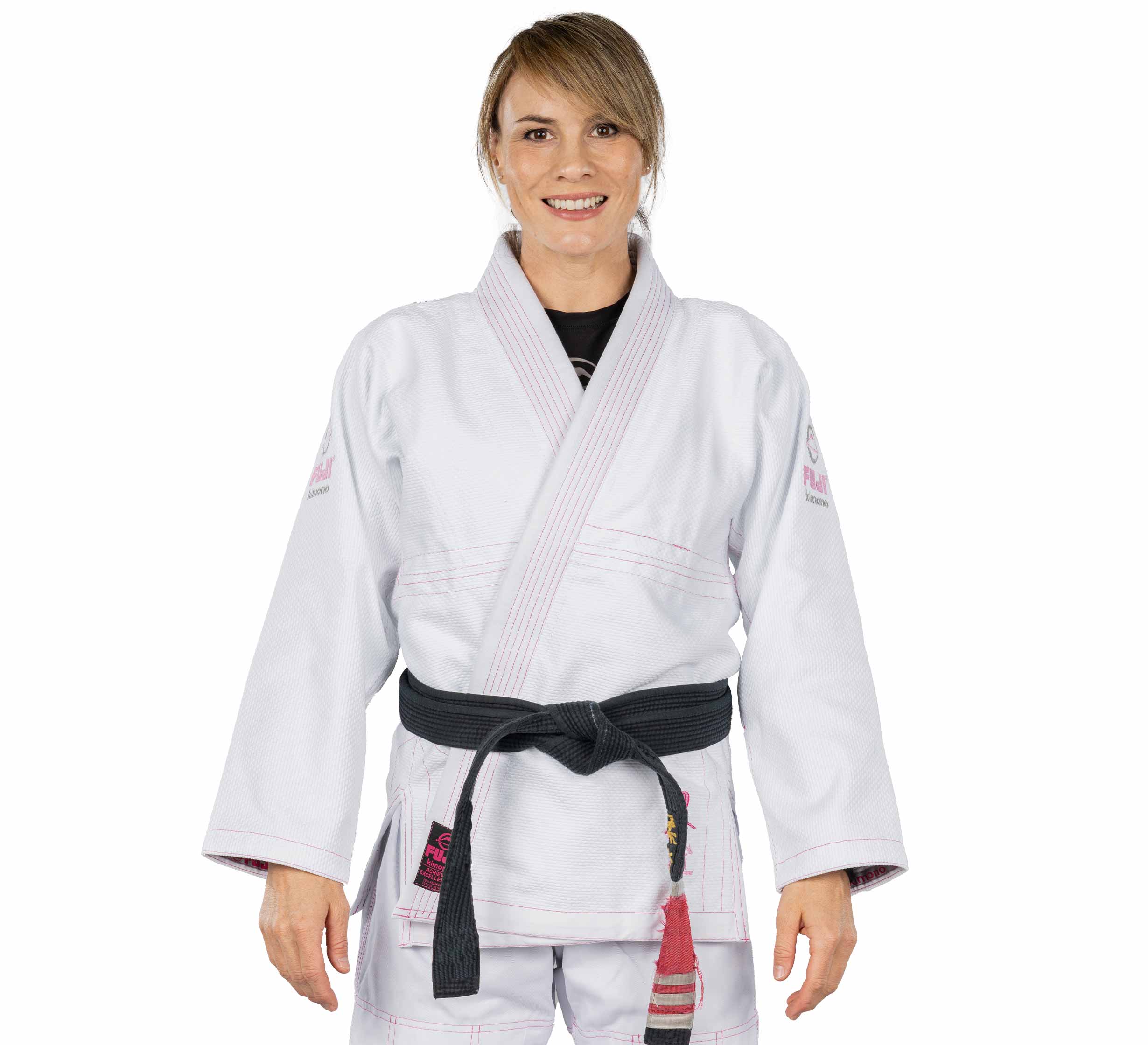 A woman stands facing forward and smiling, wearing the Blossom Womens Jiu Jitsu Gi White and a black belt, with her hands relaxed at her sides.