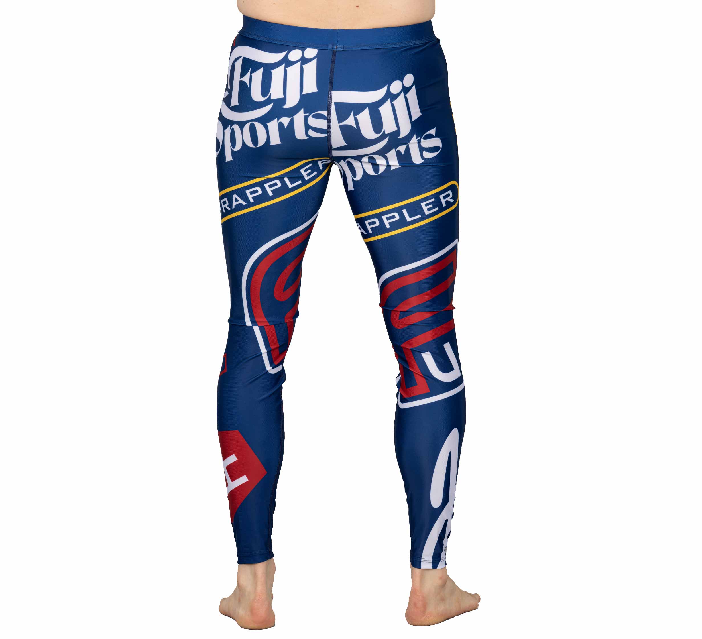A person stands barefoot, shown from the waist down, wearing XTR Extreme V1 Grappling Spats Navy featuring bold red, white, and yellow Fuji Sports and Grappler logos on the back and legs.