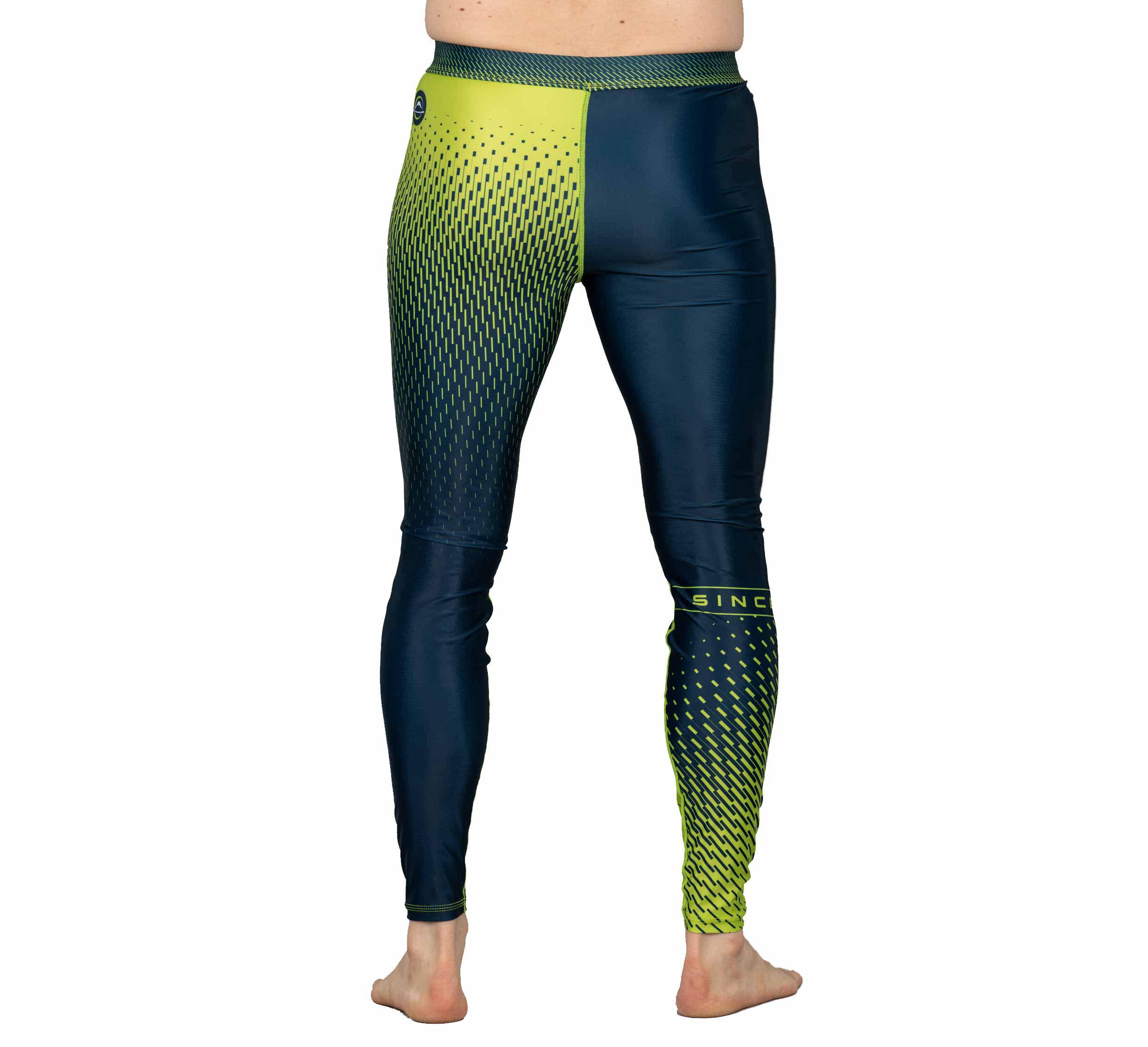 A person stands barefoot, shown from the back against a white background, wearing Match Grappling Spats Navy—navy blue leggings with a yellow geometric gradient pattern.