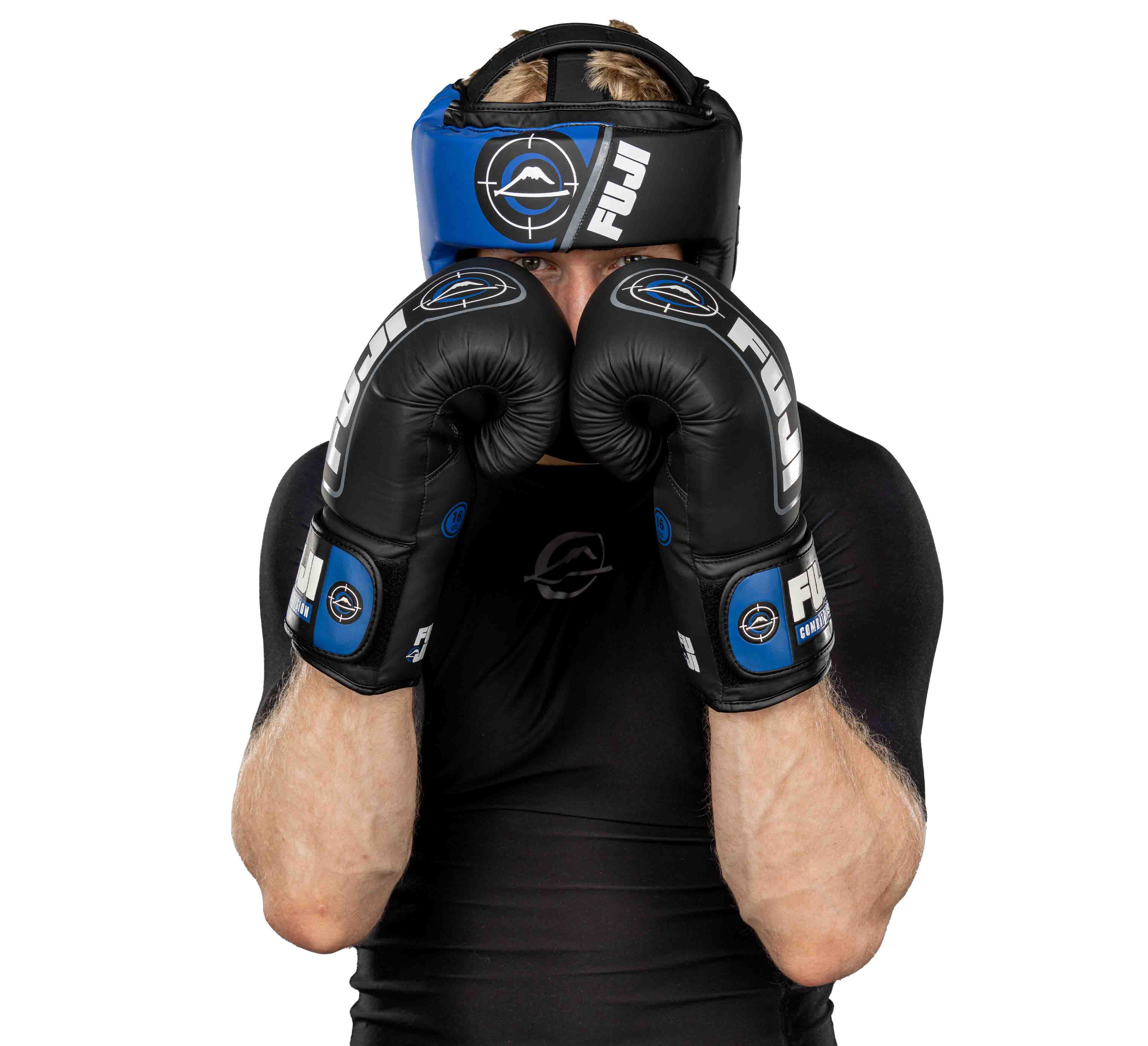 Wearing black and blue FUJI boxing gloves and the Precision Striking Headgear, a person in a black athletic shirt stands in a defensive pose with both gloves raised, set against a white background.