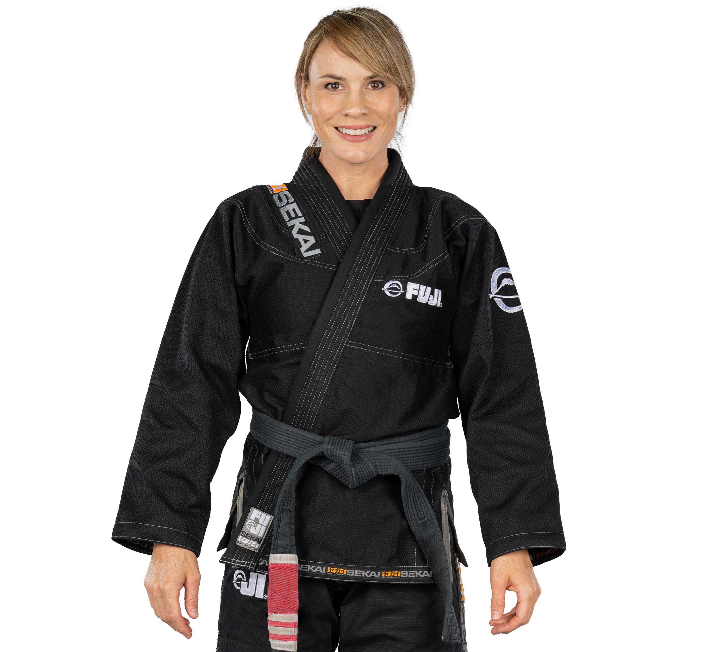 A person smiles while wearing the Sekai 2.0 Womens BJJ Gi Black with Fuji and Seka logos, paired with a black belt featuring red and white stripes, standing against a plain white background.
