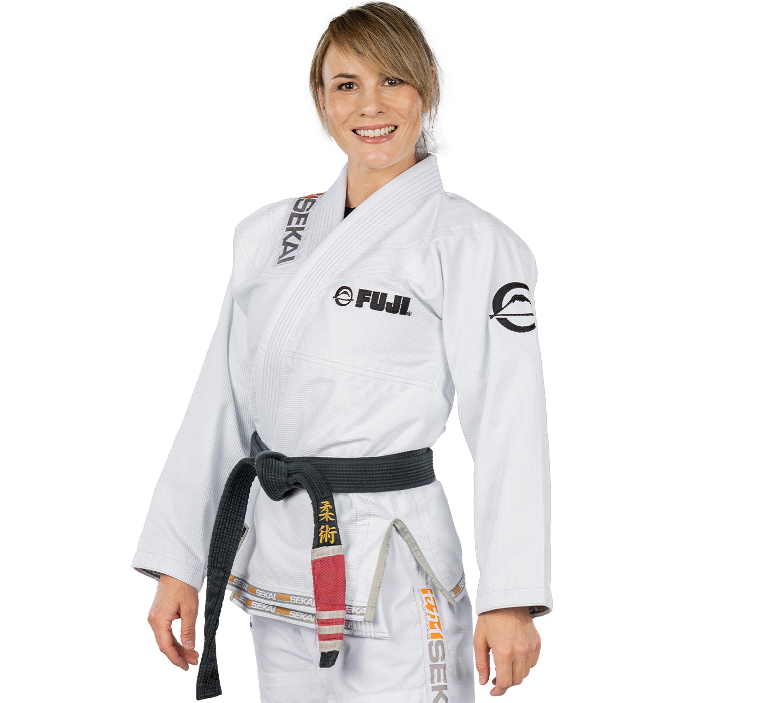 A woman in a white Sekai 2.0 Womens BJJ Gi with a black belt stands smiling. The gi features FUJI and SEKAI patches plus Japanese characters, shown against a plain white background.
