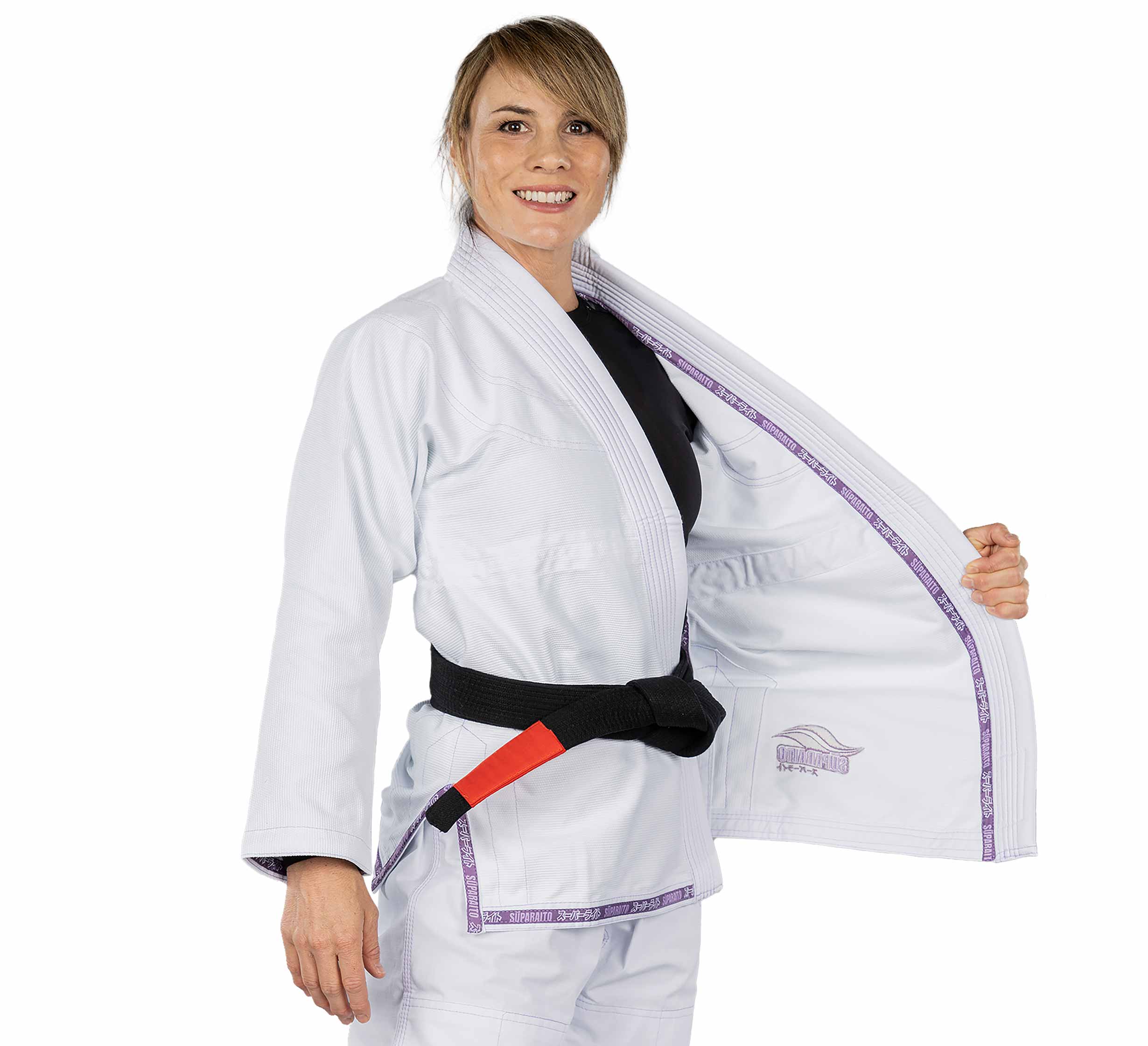 A smiling woman wears the Suparaito Womens BJJ Gi Purple, a white Brazilian Jiu-Jitsu gi with purple trim and a black belt. She holds one side open to reveal the interior, standing against a plain white background.
