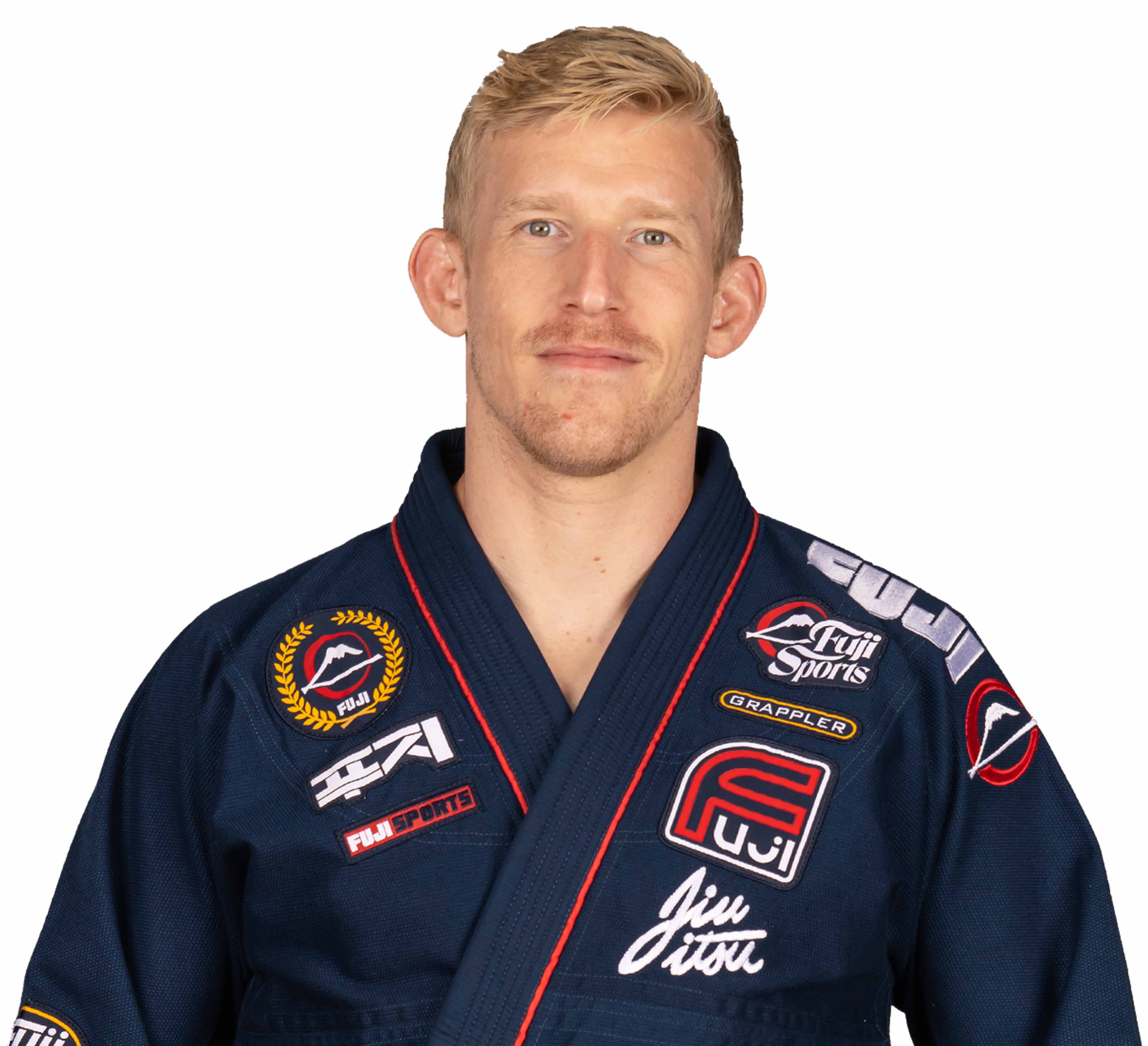 A man with short blond hair wears the Suparaito BJJ Gi XTR Edition Navy, featuring various patches and logos, standing and facing the camera with a neutral expression.