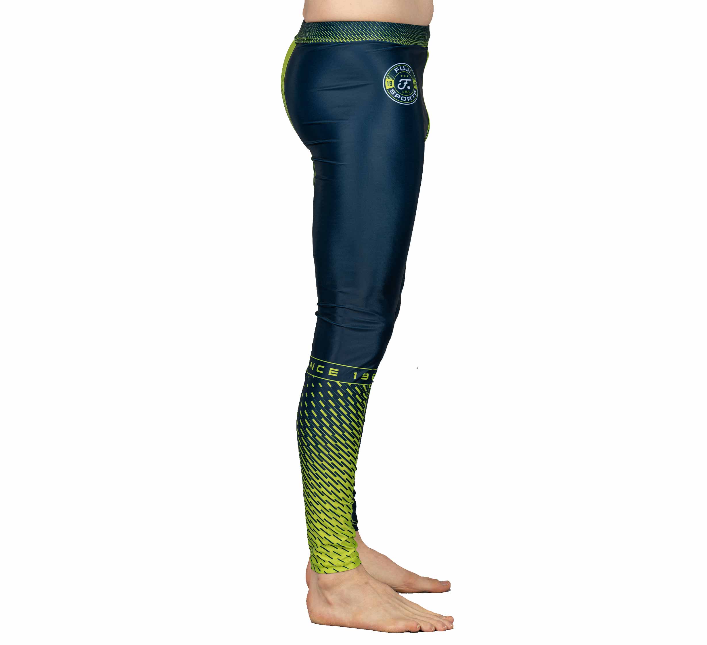 A person stands sideways, barefoot, against a white background wearing Match Grappling Spats Navy—athletic leggings featuring navy blue and neon yellow geometric patterns.