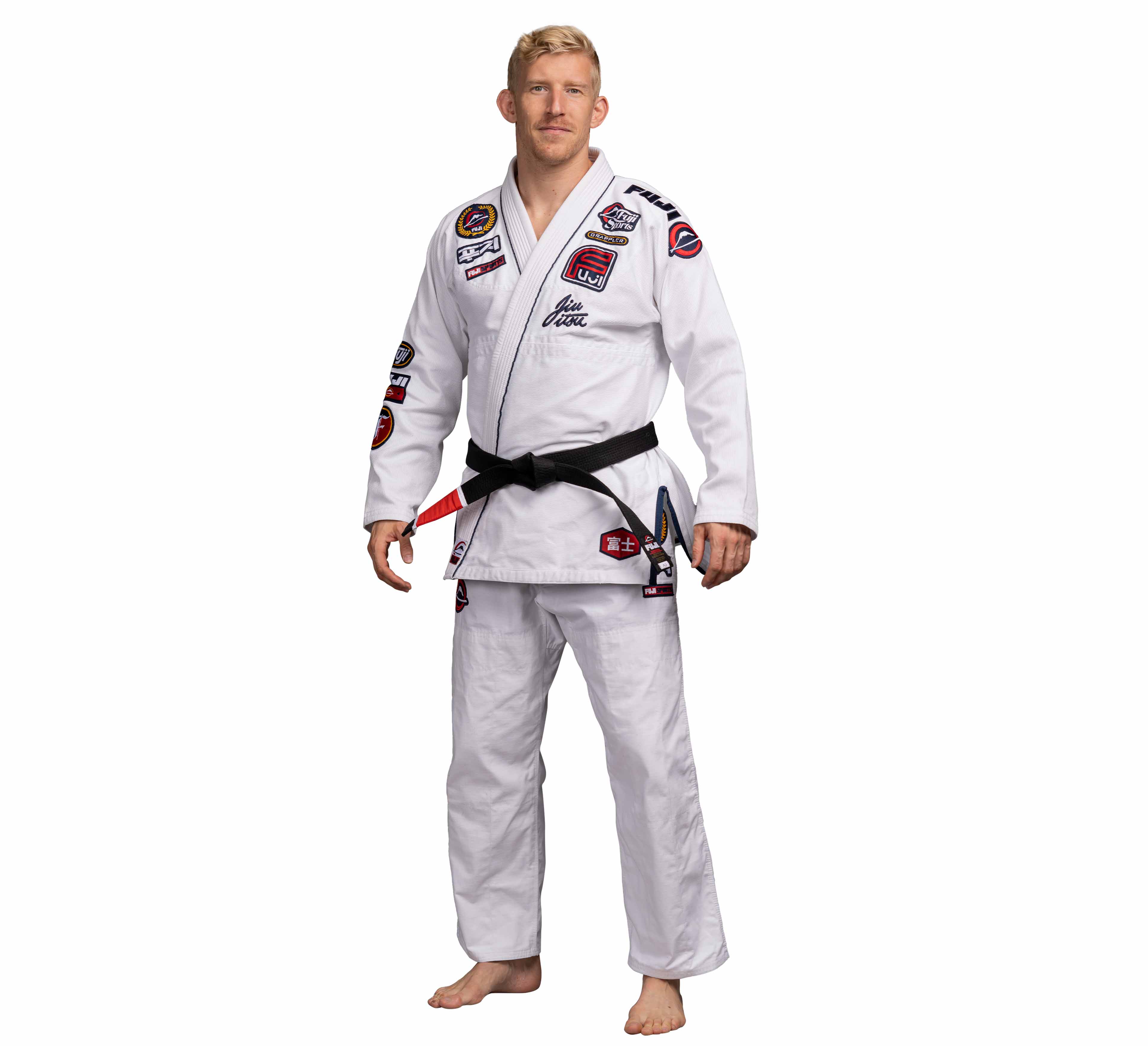 A man stands barefoot against a white background, wearing the Suparaito BJJ Gi XTR Edition White, featuring various patches and a black belt.