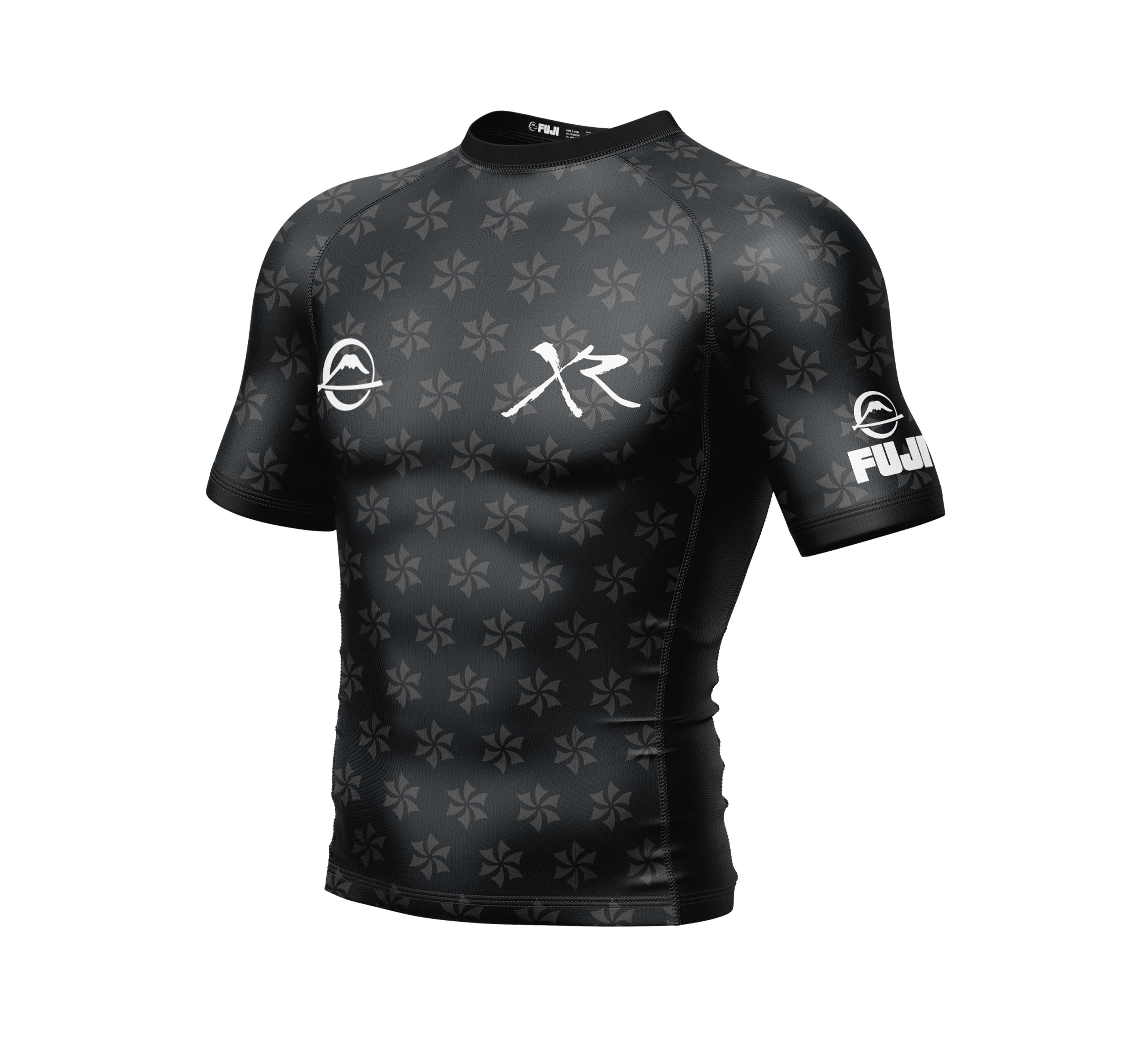 The Xande Comp Short Sleeve Rashguard Black features a subtle star-like pattern, white logos on the chest and sleeves, and FUJI branding on the left sleeve. Displayed against a plain white background.