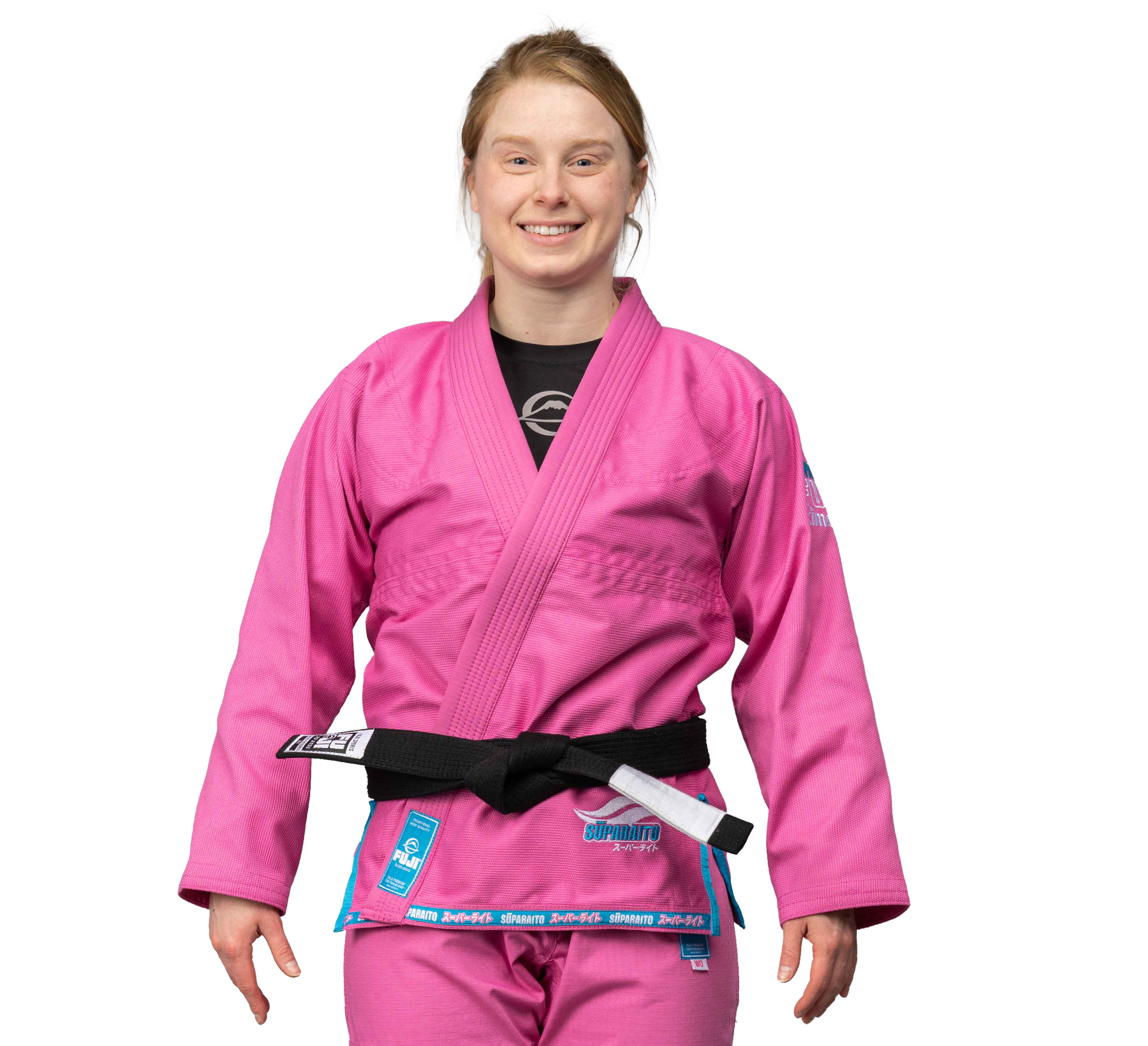 A woman smiles at the camera wearing the Suparaito Womens BJJ Gi in pink with a black belt, standing against a white background.