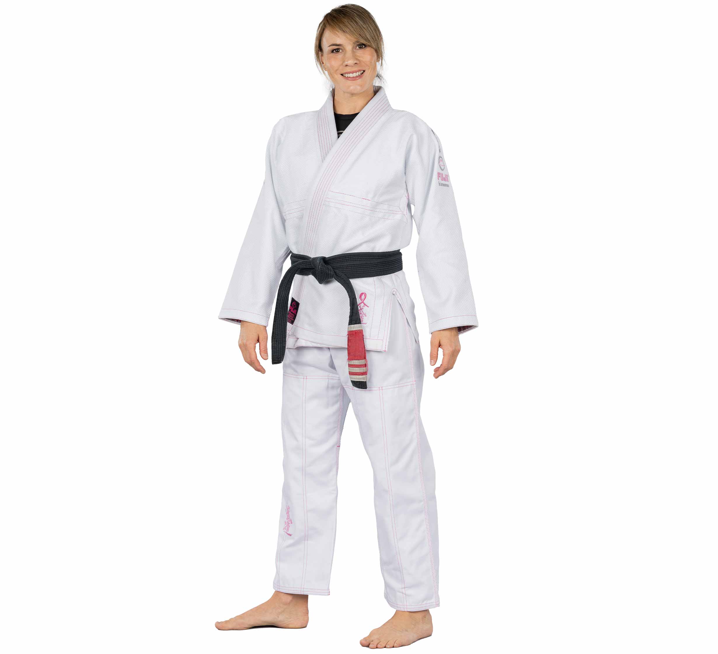 A smiling woman stands barefoot, facing forward with relaxed hands by her sides, wearing the Blossom Womens Jiu Jitsu Gi White and a black belt on a plain white background.