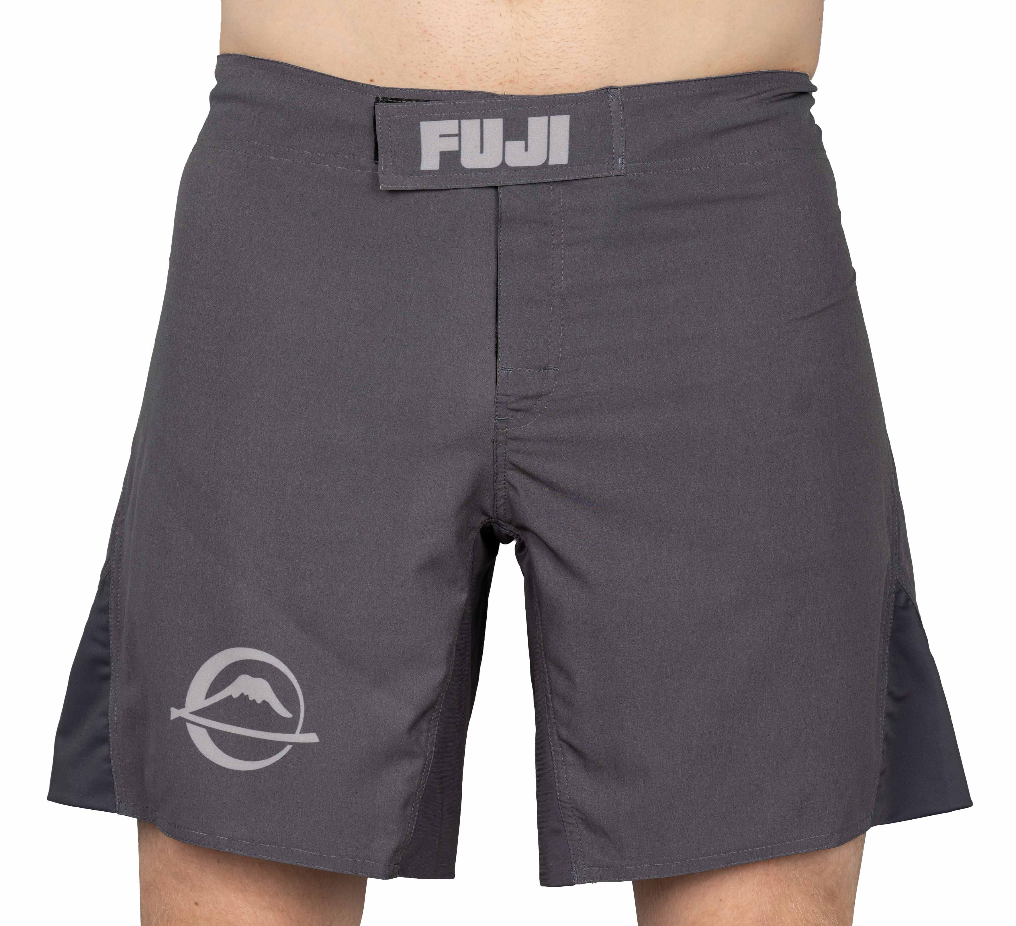 A person wearing grey Baseline Fight Shorts with a Velcro waistband labeled FUJI and a mountain logo on the left leg. The shorts feature black side panels and are above-the-knee length.