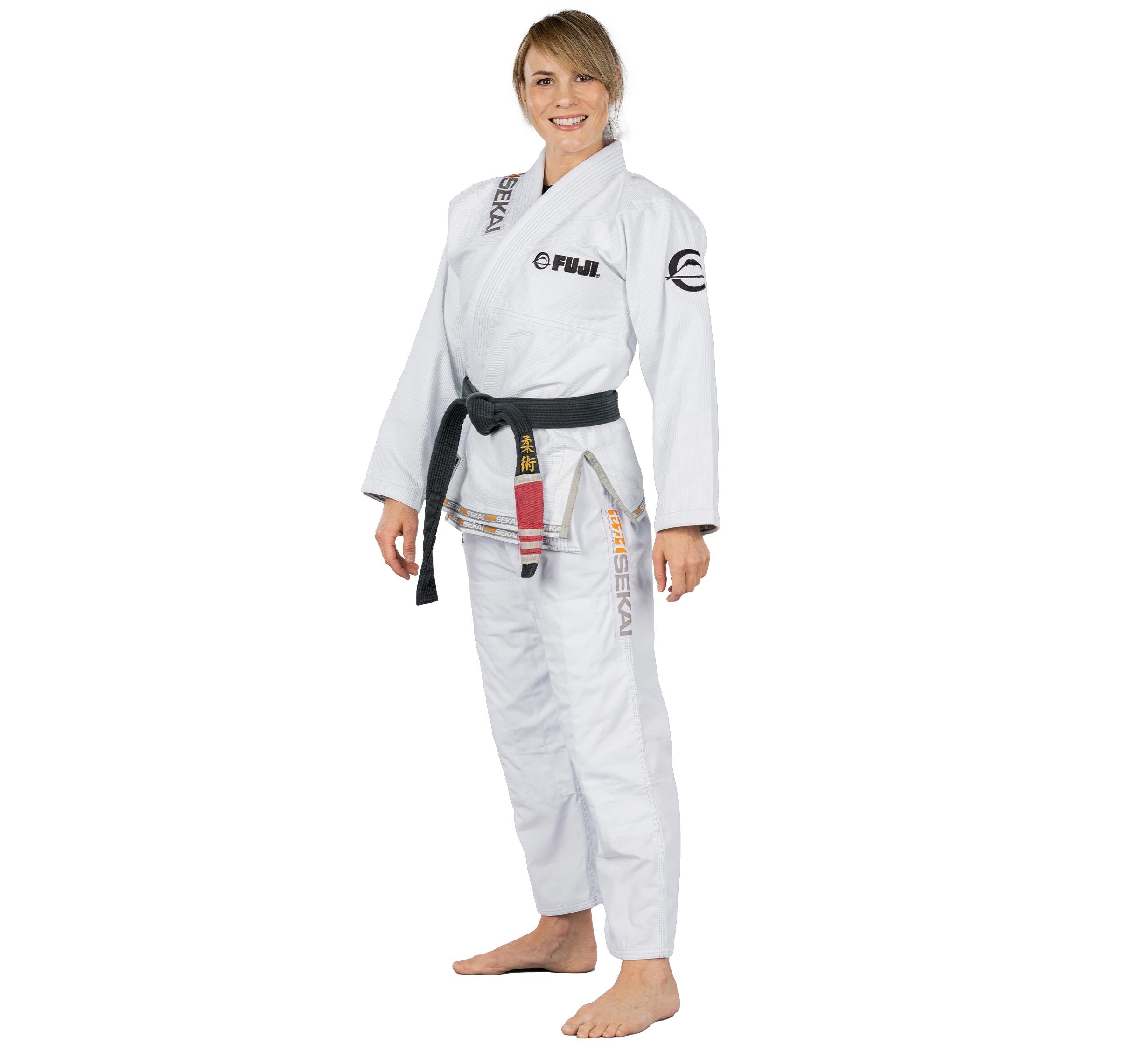 A woman stands barefoot, smiling, and wearing the Sekai 2.0 Womens BJJ Gi White with a black belt on a white background.