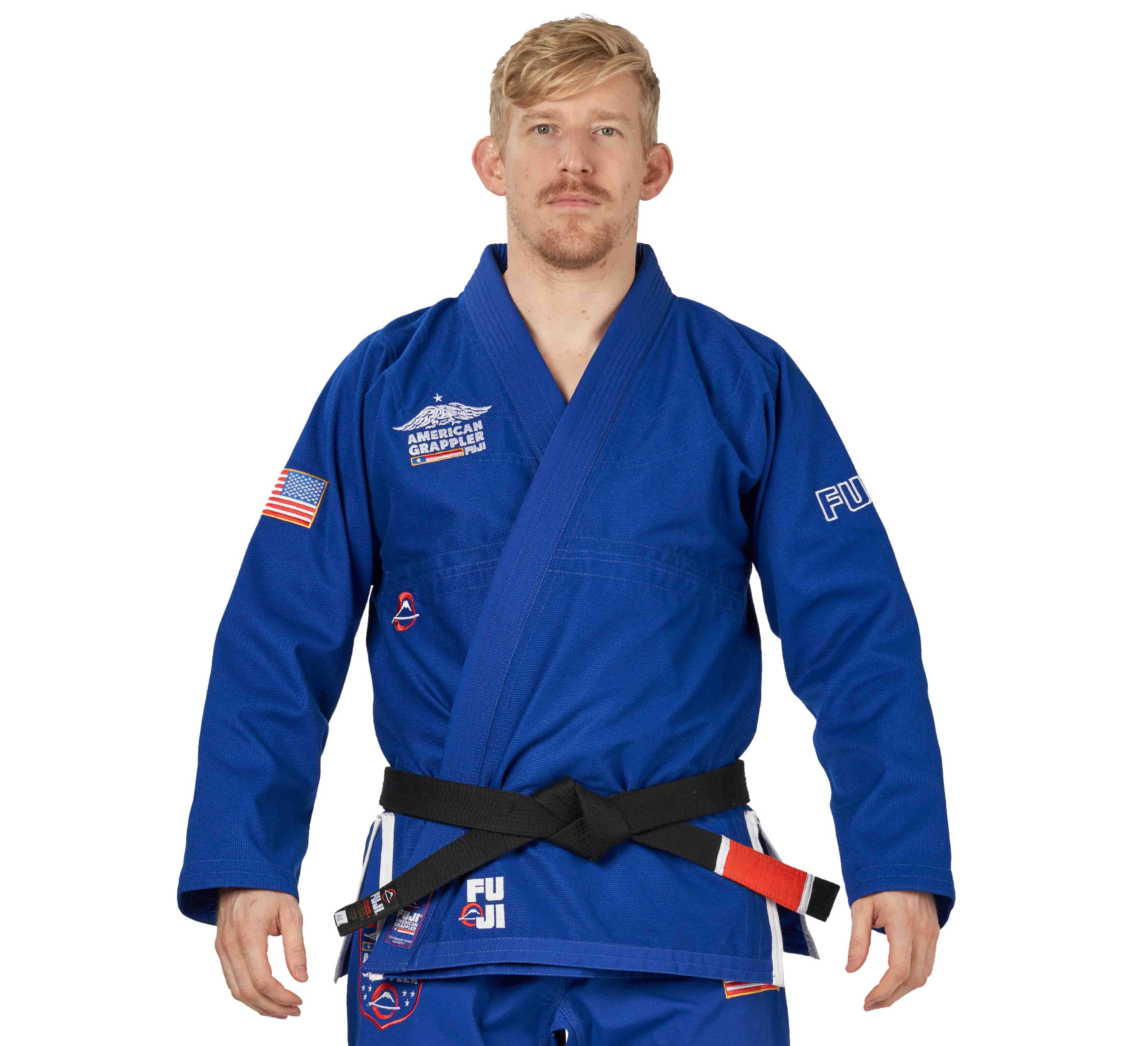 A man wearing the Suparaito BJJ Gi American Grappler Blue with various patches and a black belt stands facing forward against a white background.