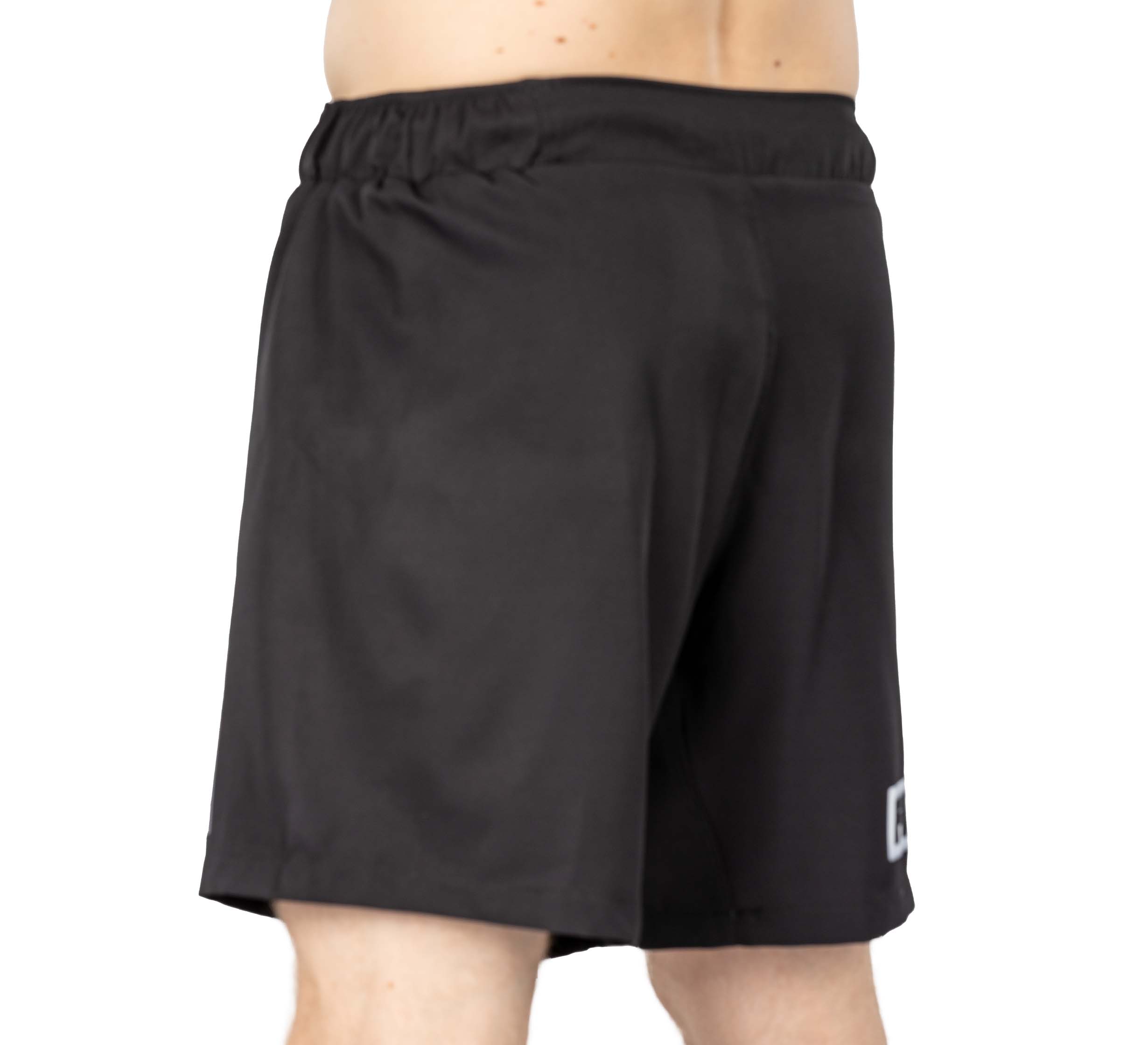 A person wearing Ultimate Grappling Shorts Black with an elastic waistband, viewed from the side and waist down against a plain white background.