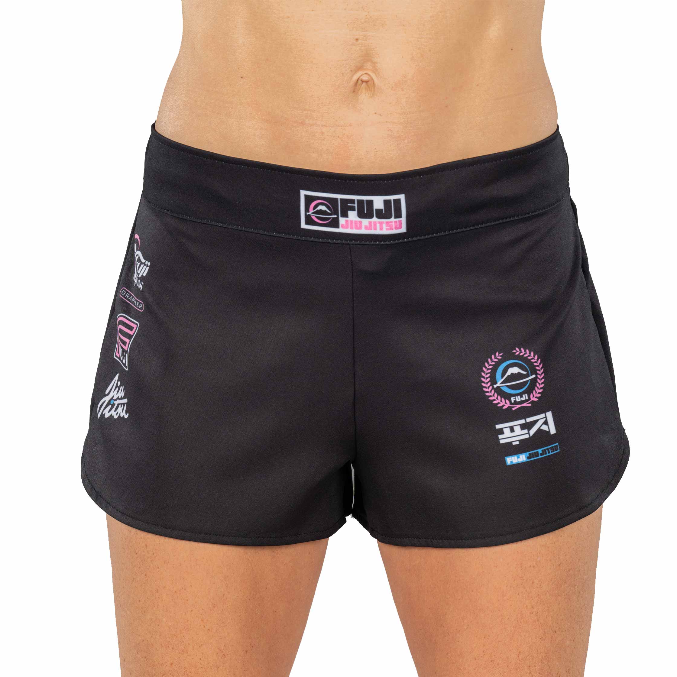 A person wearing XTR Extreme Womens Grappling Fight Shorts Pink, featuring Fuji Jiu Jitsu and various white and pink logos on black fabric. The photo is cropped to show only the waist and upper thighs.