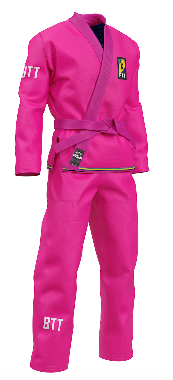 The BTT Standard Women's Gi in pink features a purple belt, BTT text on the sleeve and pant leg, and a yellow and black patch on the chest. Displayed on a white background.