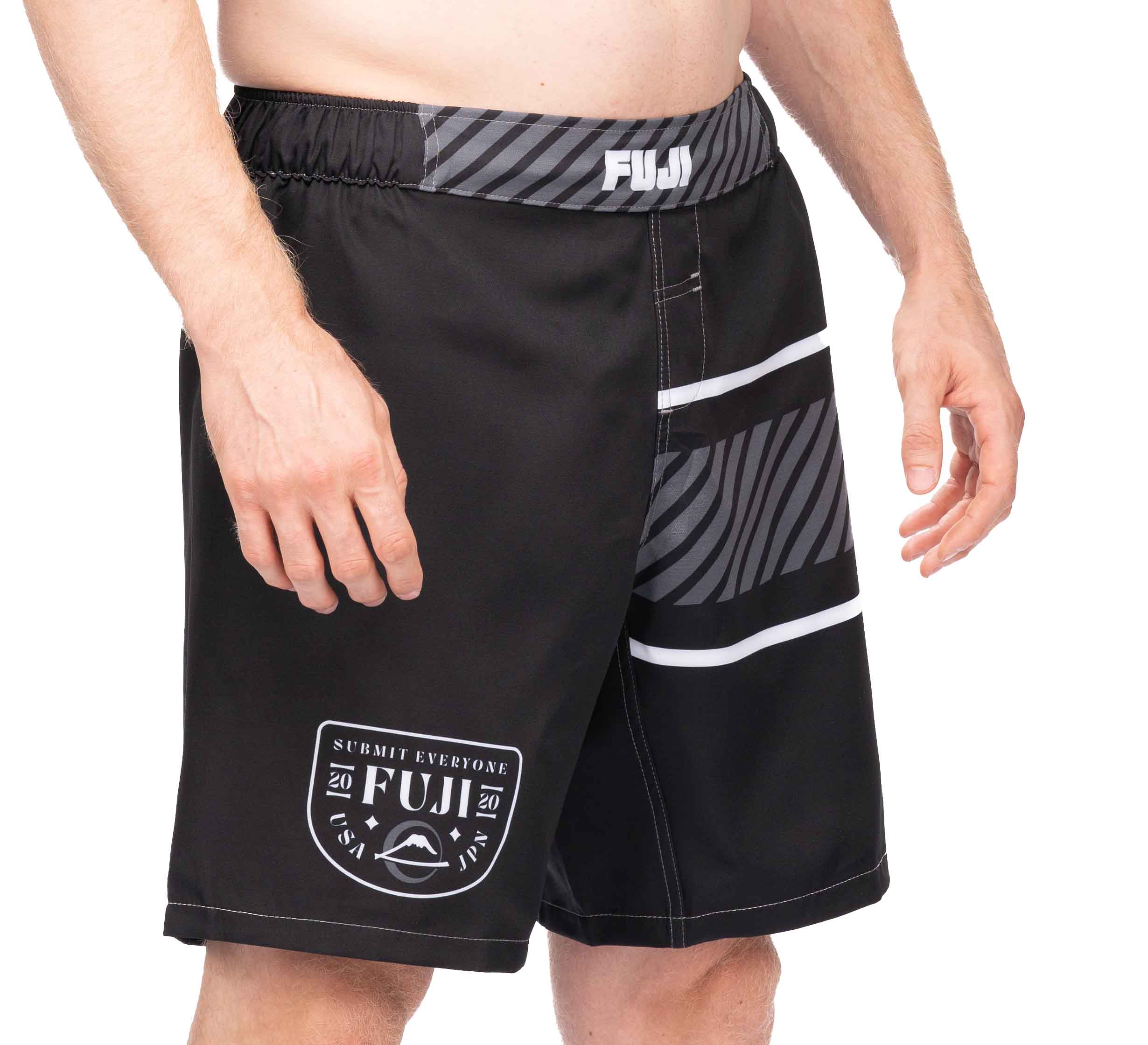 A person wears black FUJI Freestyle 2.0 Ranked Grappling Shorts with white and gray stripes, FUJI logos on the waistband and left leg, and a "Submit Everyone" patch featuring a stylized mountain and year design.