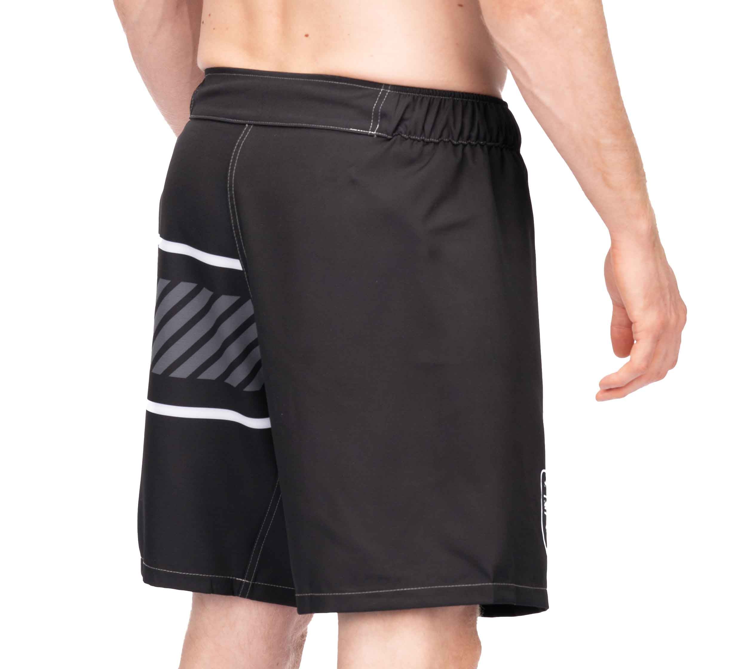 A man faces away from the camera, wearing Freestyle 2.0 Ranked Grappling Shorts featuring black fabric, a white-and-gray diagonal stripe on one side, an elastic waistband, and white stitching.