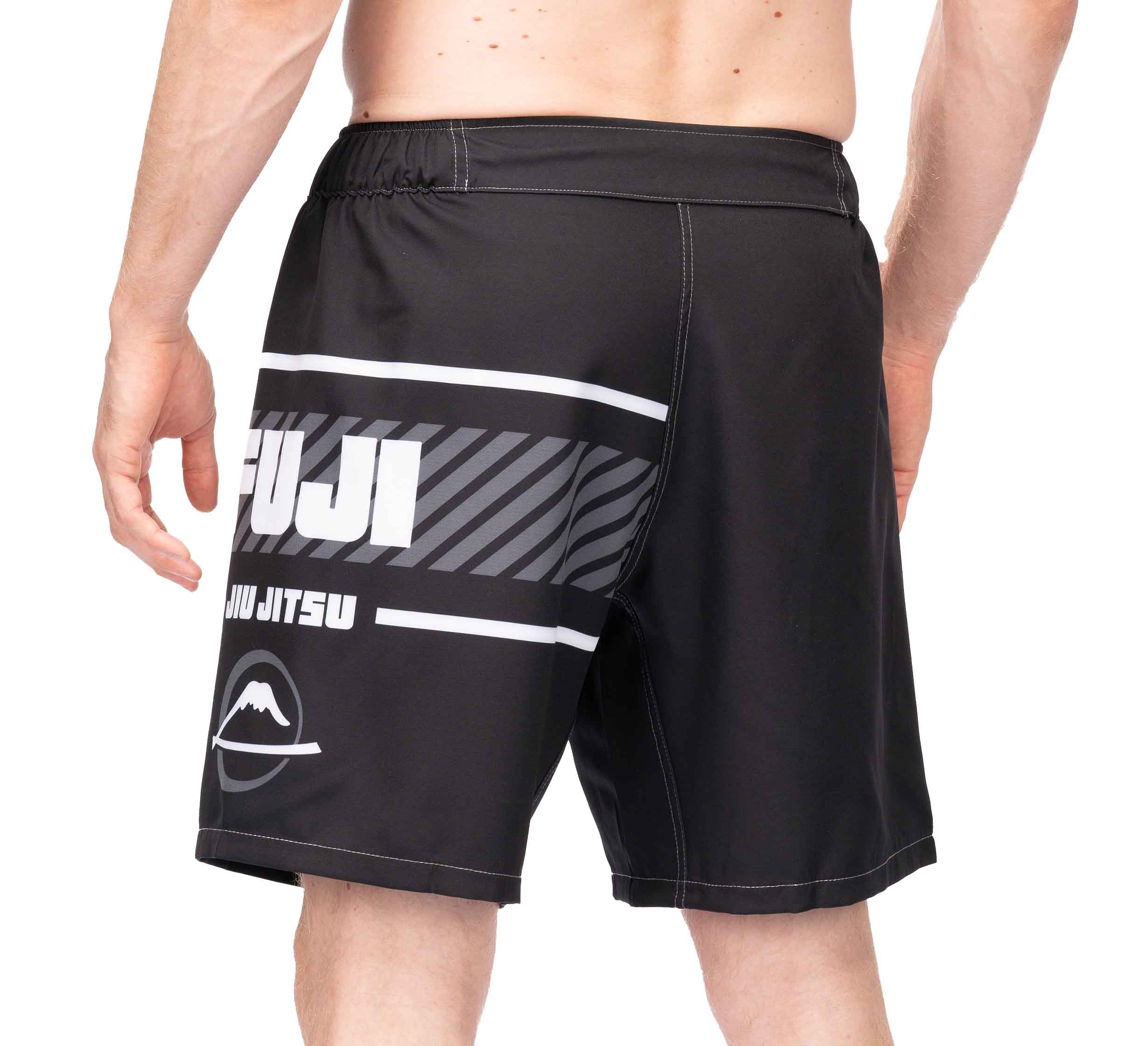 A person wearing black Freestyle 2.0 Ranked Grappling Shorts, viewed from the back. The shorts display bold white text, stripes, and a mountain logo on the lower left leg.