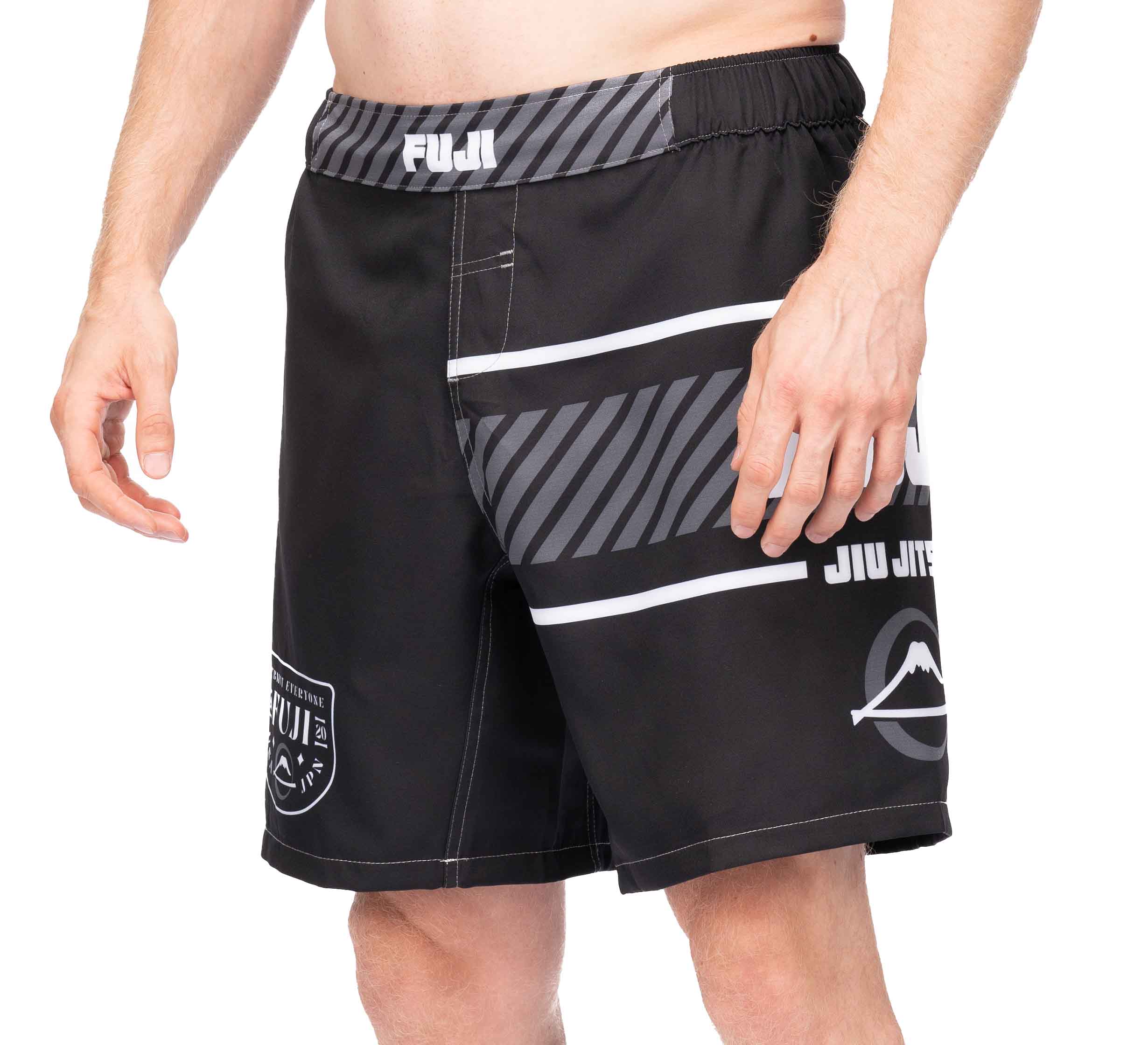 A person is wearing black Freestyle 2.0 Ranked Grappling Shorts with gray and white stripes and logos, featuring an elastic waistband and a mid-thigh length.