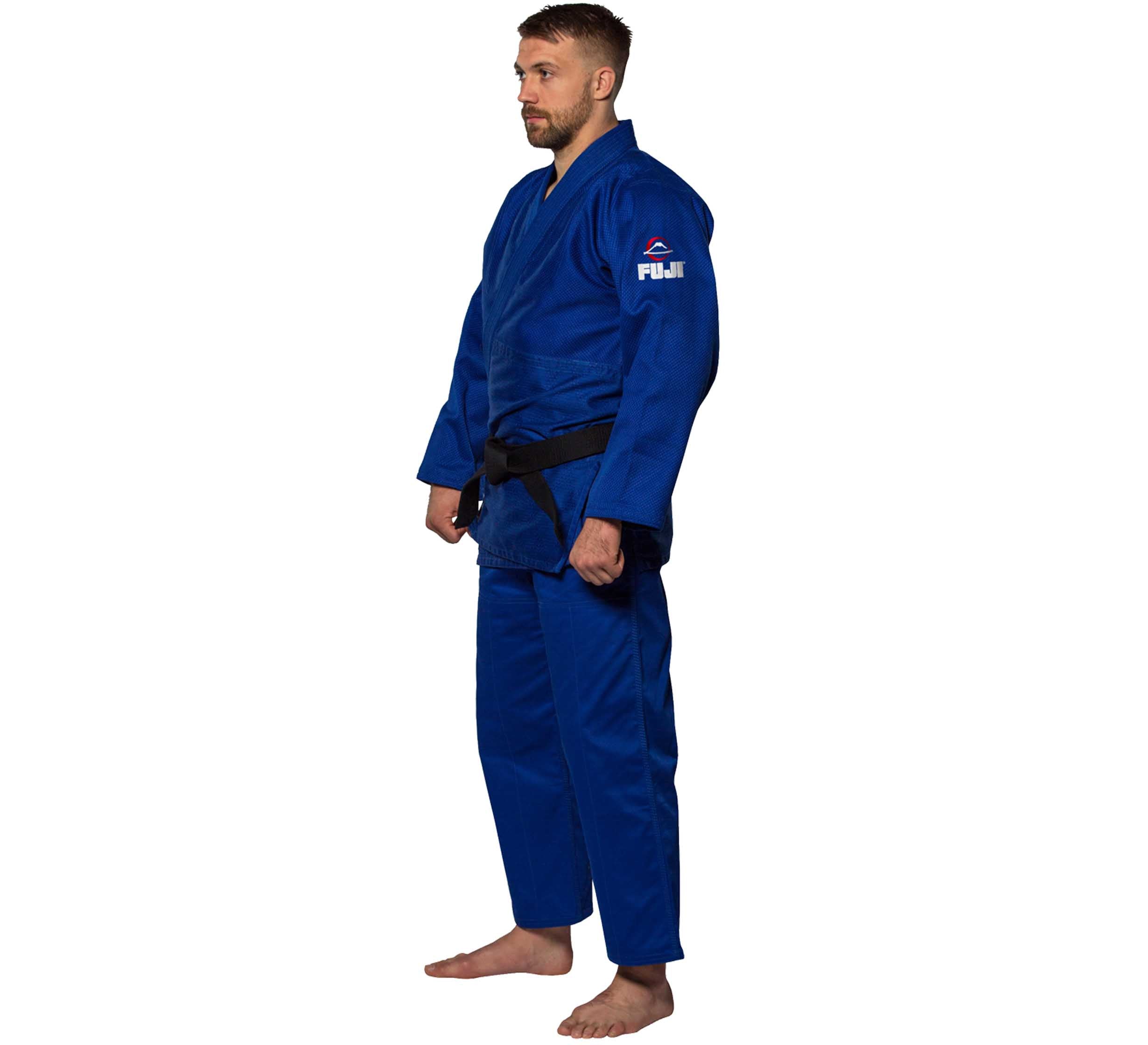 A man stands barefoot in a blue Single Weave Judo Gi with a black belt, featuring a Fuji logo on the sleeve. He is facing slightly to the left against a white background.