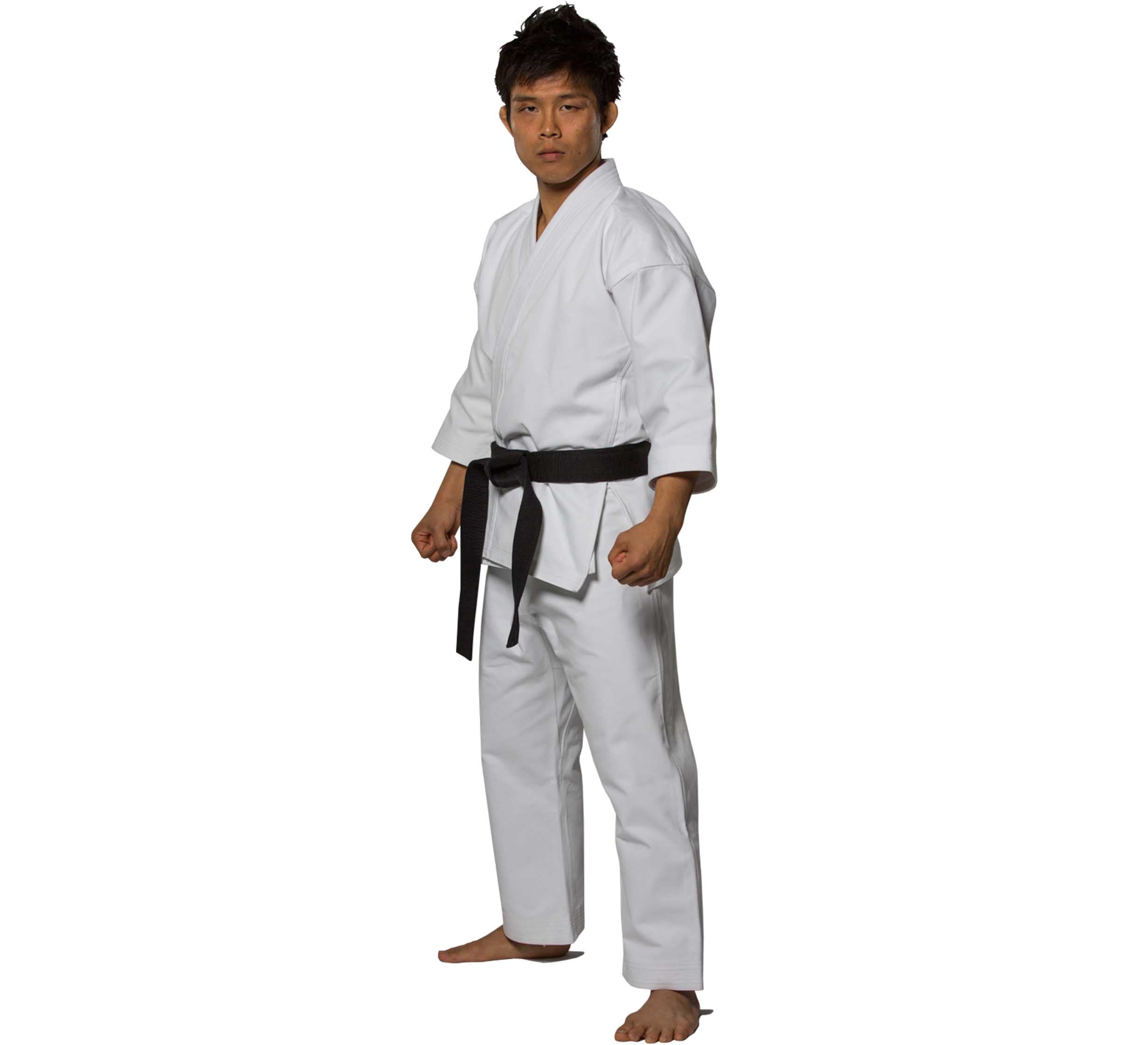 A person in the Advanced Brushed Karate Gi and black belt stands barefoot in a ready stance against a plain white background.