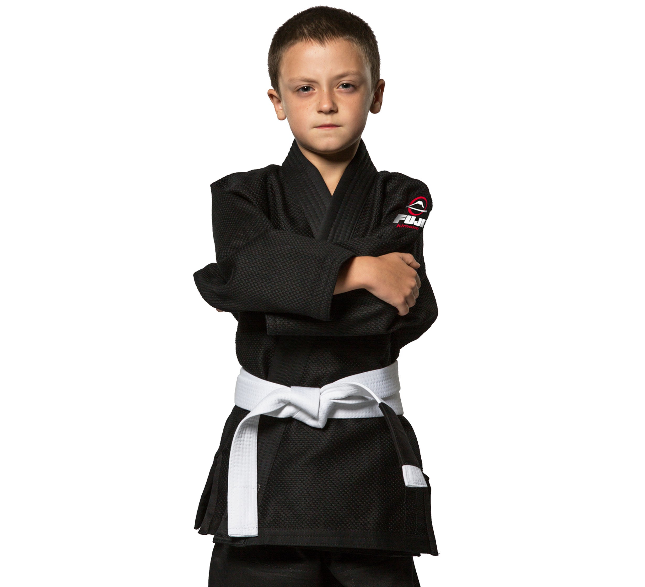 A young boy wears the All Around Kids BJJ Gi in black with a white belt, standing with arms crossed and looking directly at the camera against a white background.