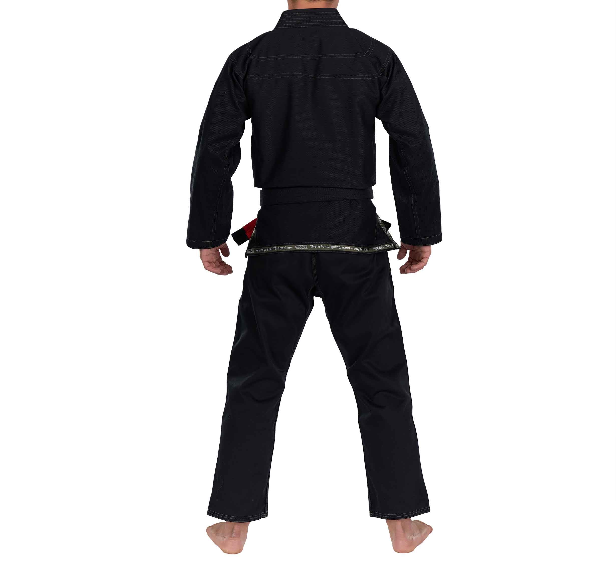 A barefoot person stands facing away, wearing the Mission 22 Black Gi—a long-sleeve martial arts uniform with pants and a belted waist.