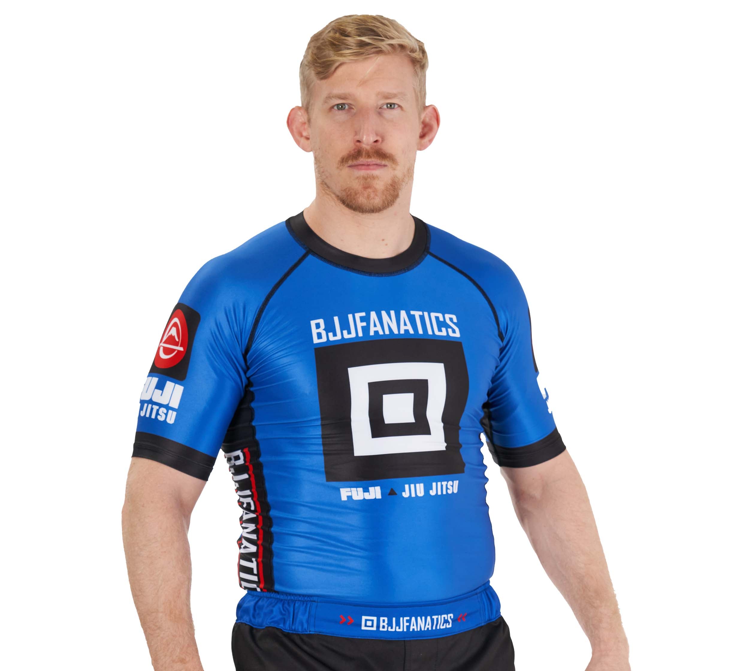 A man with short blond hair and a beard wears the BJJ Fanatics Rashguard Blue and black shorts, facing forward against a white background.