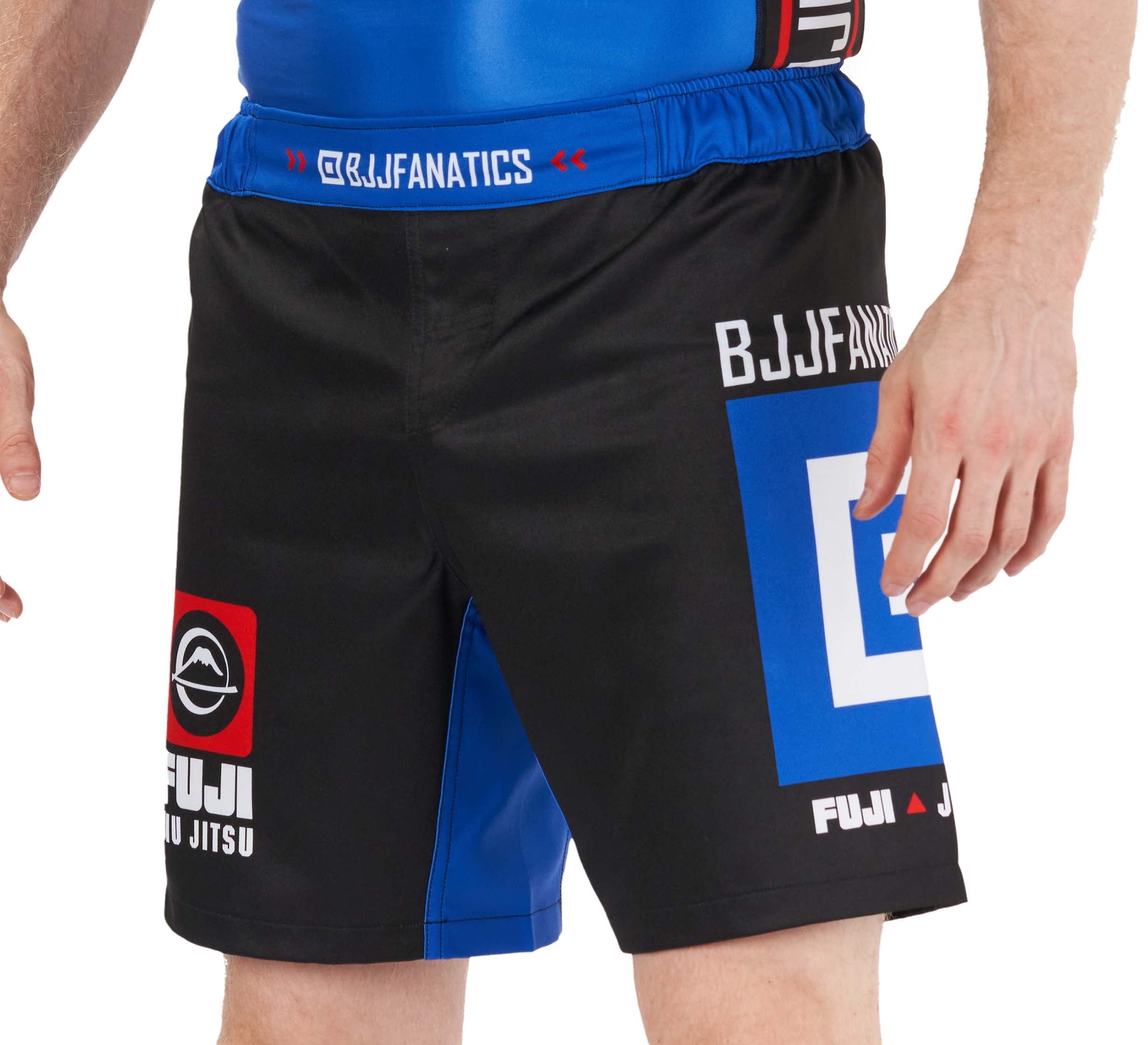 A person wearing BJJ Fanatics Lightweight Shorts Blue with “BJJFANATICS” and “FUJI JIU JITSU” logos, standing with one hand by their side.