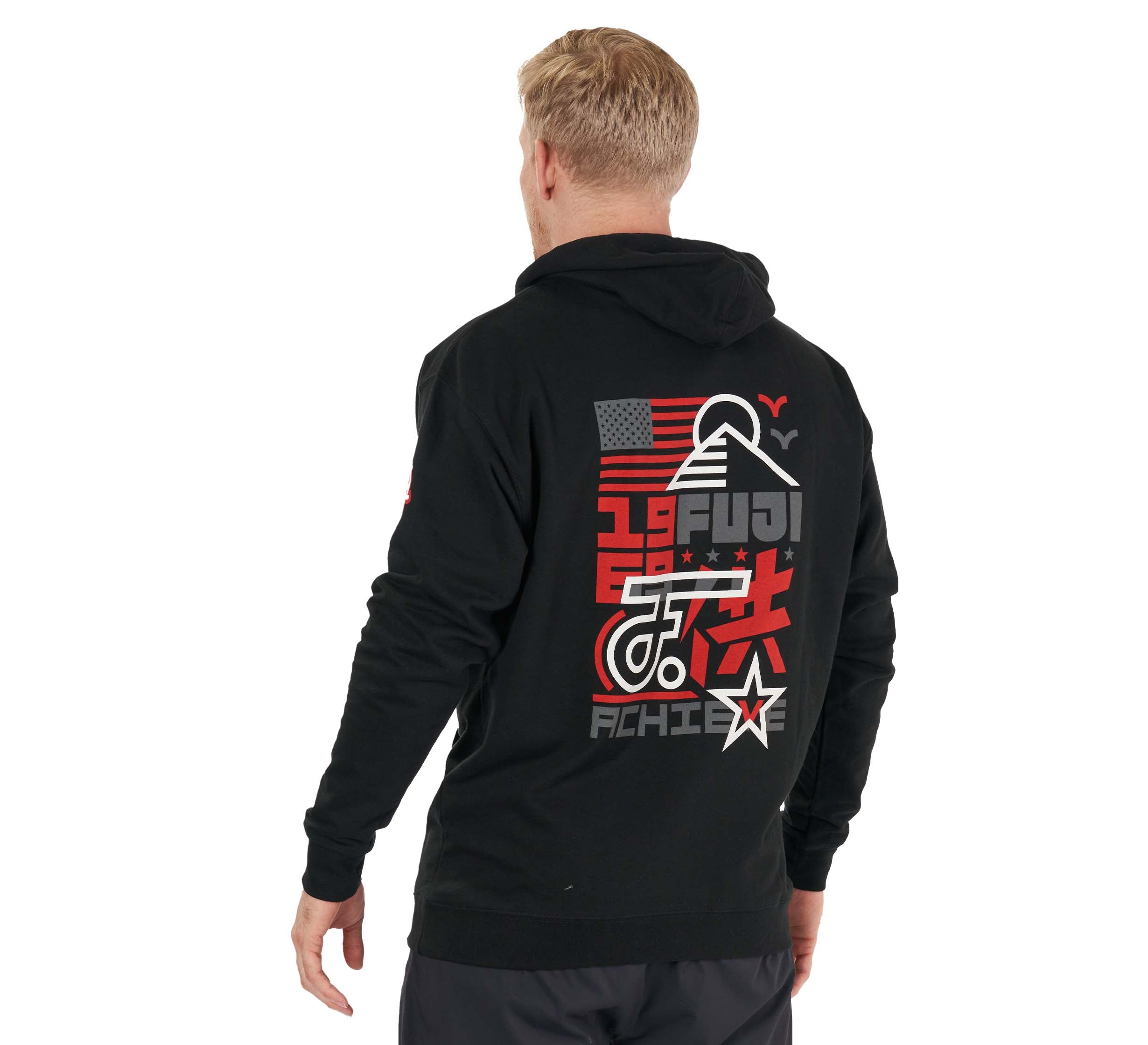 A blonde man, seen from behind, wears the Achieve Hoodie Black featuring a bold back graphic with red, gray, and white text, abstract shapes, a U.S. flag, and the word "ACHIEVE.