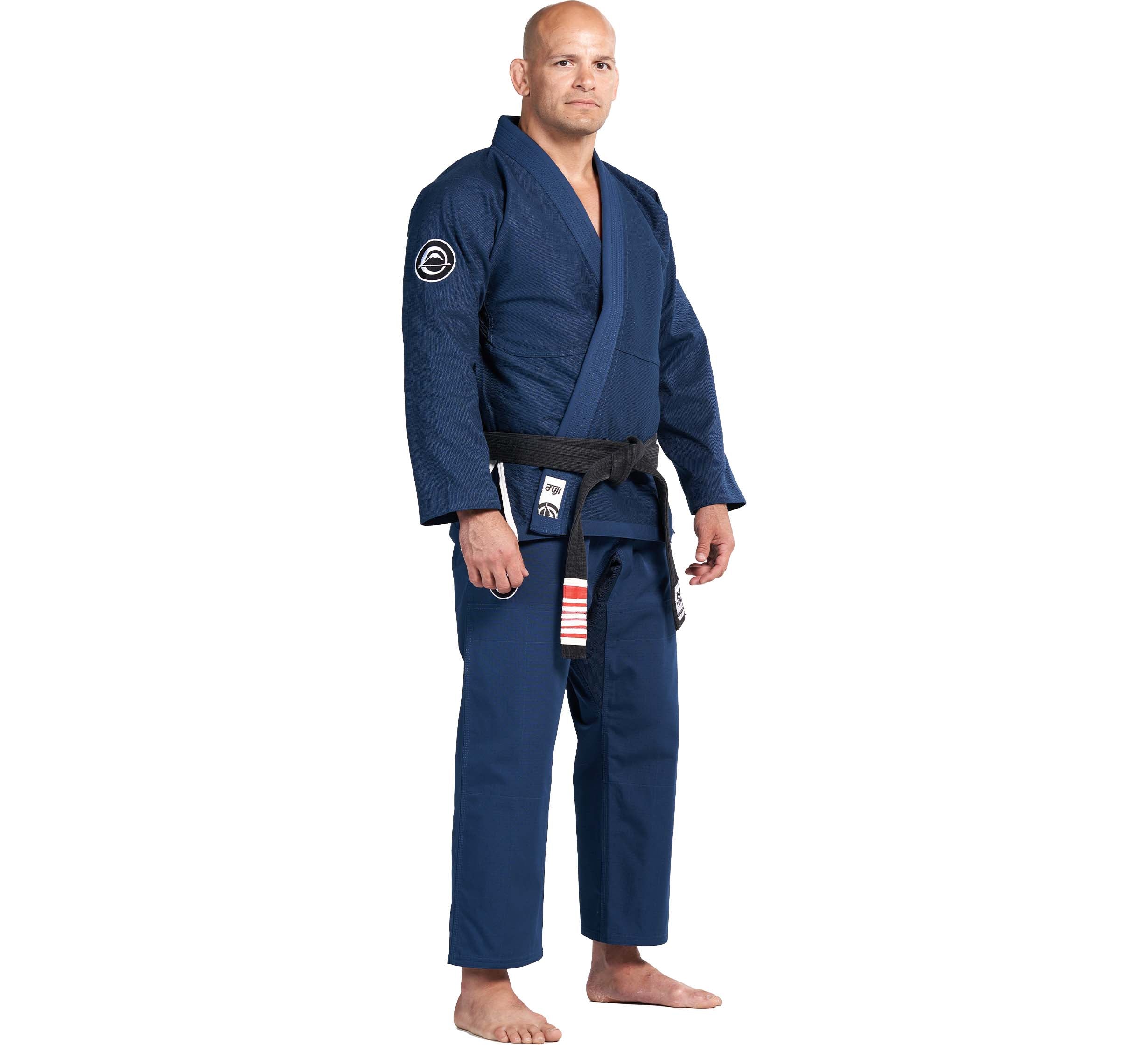 A man stands barefoot wearing the Flow-Tech BJJ Gi Navy with a striped and patched black belt, facing forward against a plain white background.