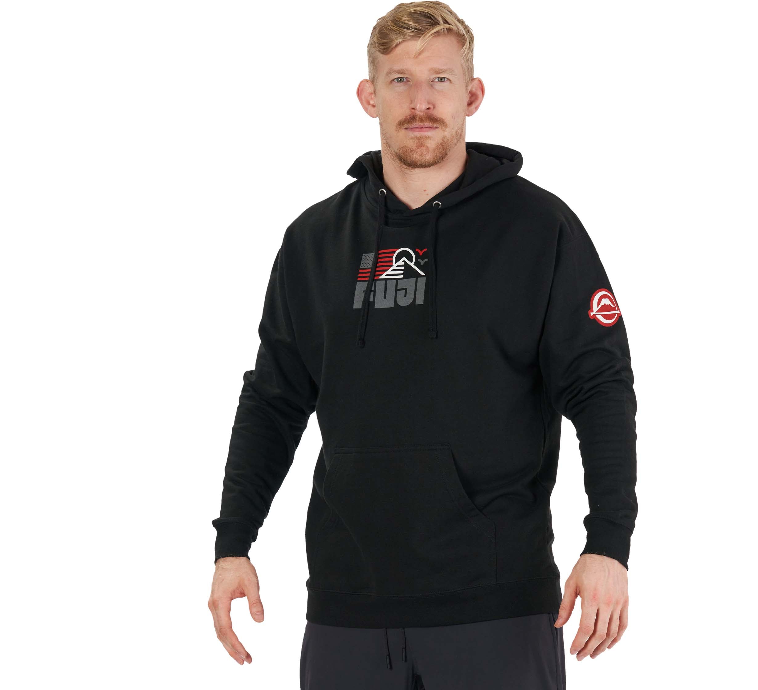 A man with short blond hair and a beard is wearing the Achieve Hoodie Black, featuring a graphic logo and black drawstrings, while standing and facing forward against a plain white background.