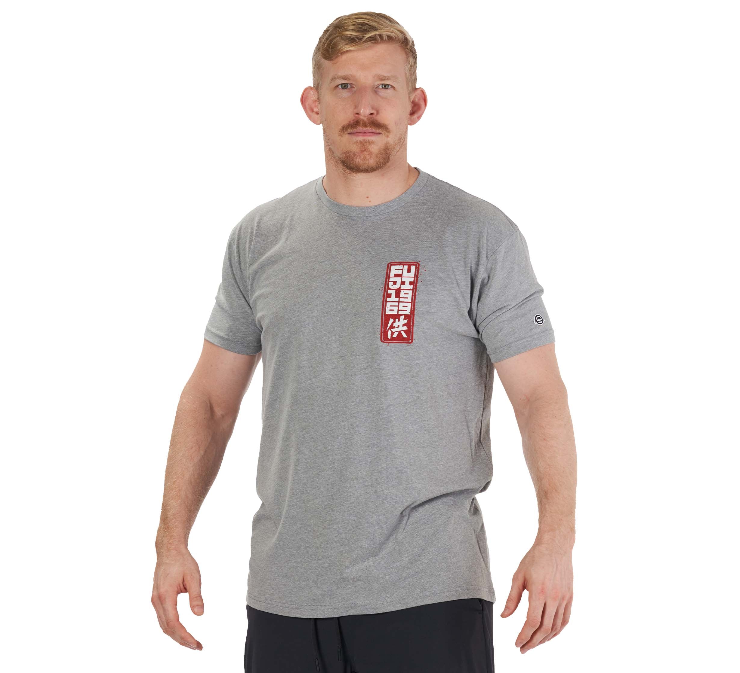 A man with short blond hair and a beard wears the Prepare For Battle T-Shirt Heather Grey, featuring a vertical red and white rectangular graphic on the chest, paired with black shorts against a plain white background.