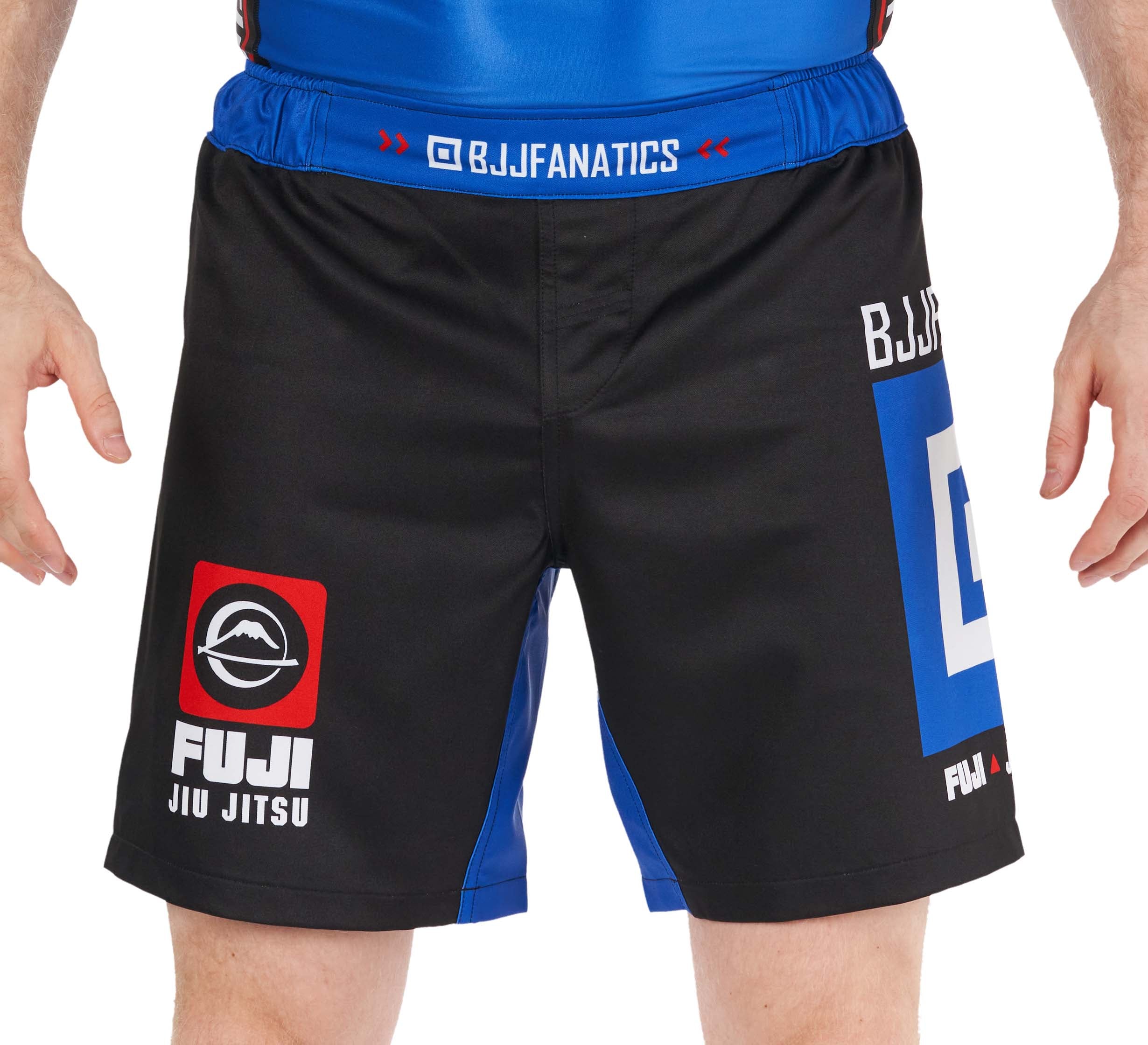 A person wearing BJJ Fanatics Lightweight Shorts Blue, featuring black and blue colors and logos, stands with arms relaxed at their sides.