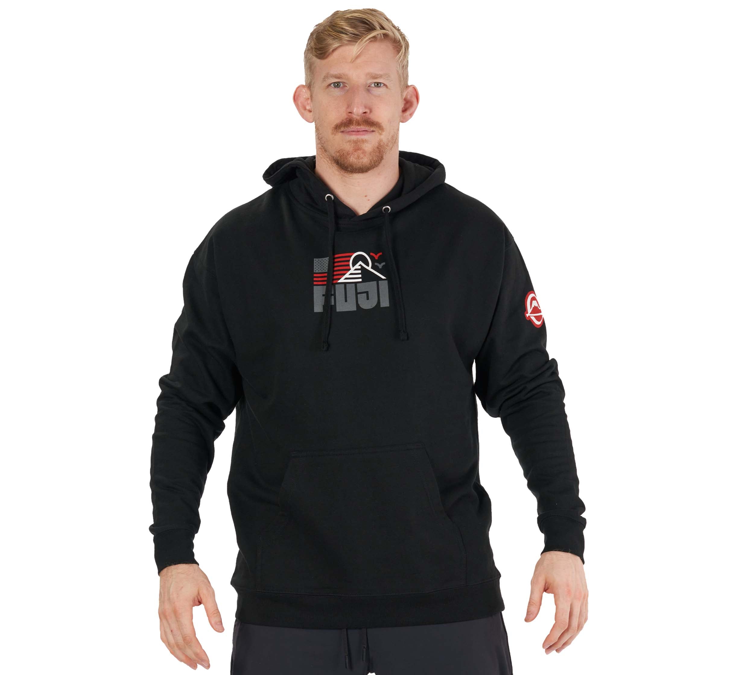 A man with short blond hair and a beard stands with his hands at his sides, wearing the Achieve Hoodie Black featuring a red and gray chest graphic and a white logo on the left sleeve.