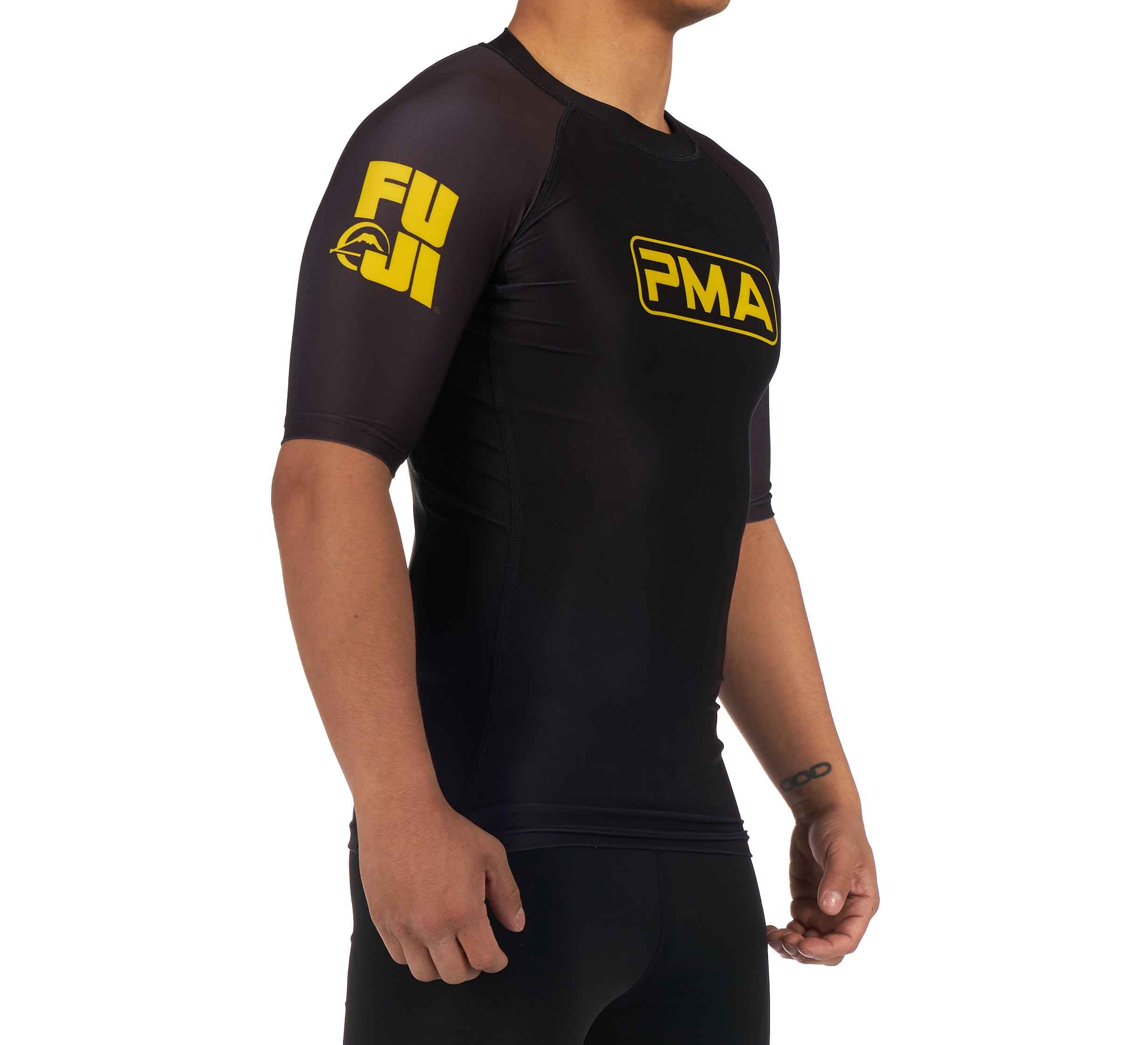 A child models the Premier Martial Arts Short Sleeve Kids Rashguard—black with yellow FUJI text on the left sleeve and a yellow PMA logo on the chest—against a white background.