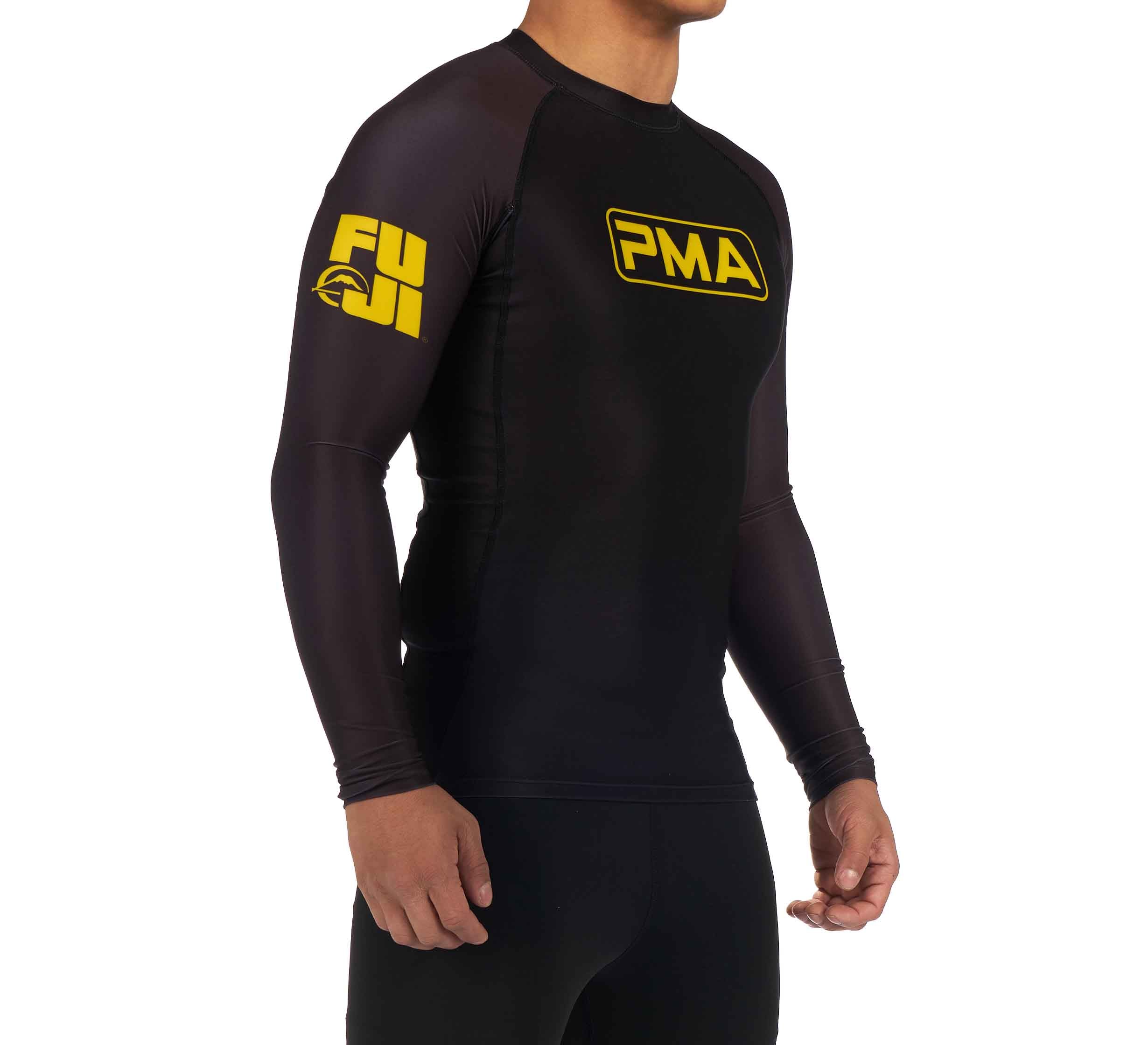 A person wearing the Premier Martial Arts Long Sleeve Rashguard, black with yellow FUJI and PMA logos on the chest and sleeve, stands against a white background with arms relaxed at their sides.